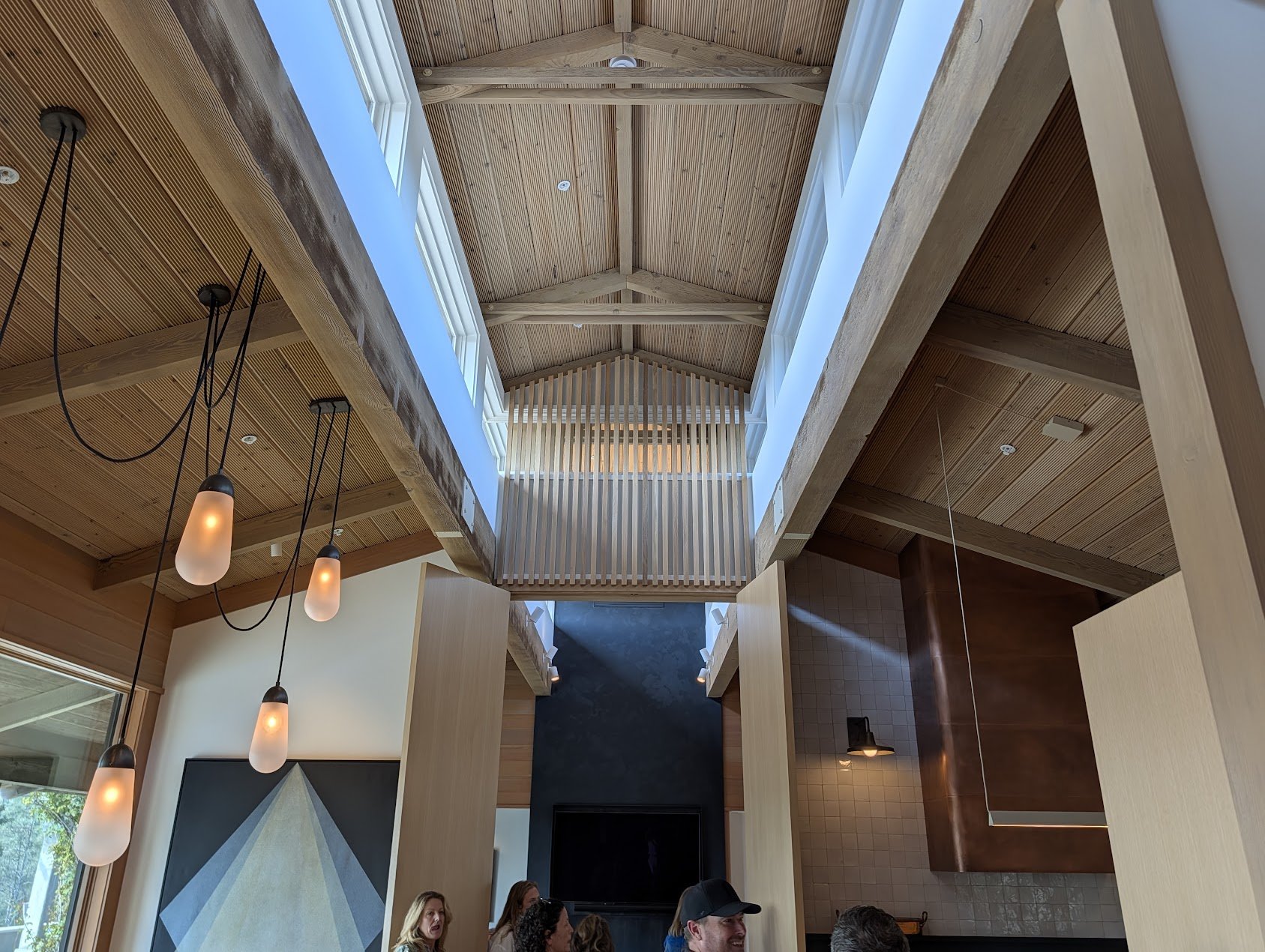 The interior of a large vaulted room, windows illuminate the cupola at the roof. Pendant lights hang on the left, wall sconces illuminate zellige tile in the kitchen to the right.