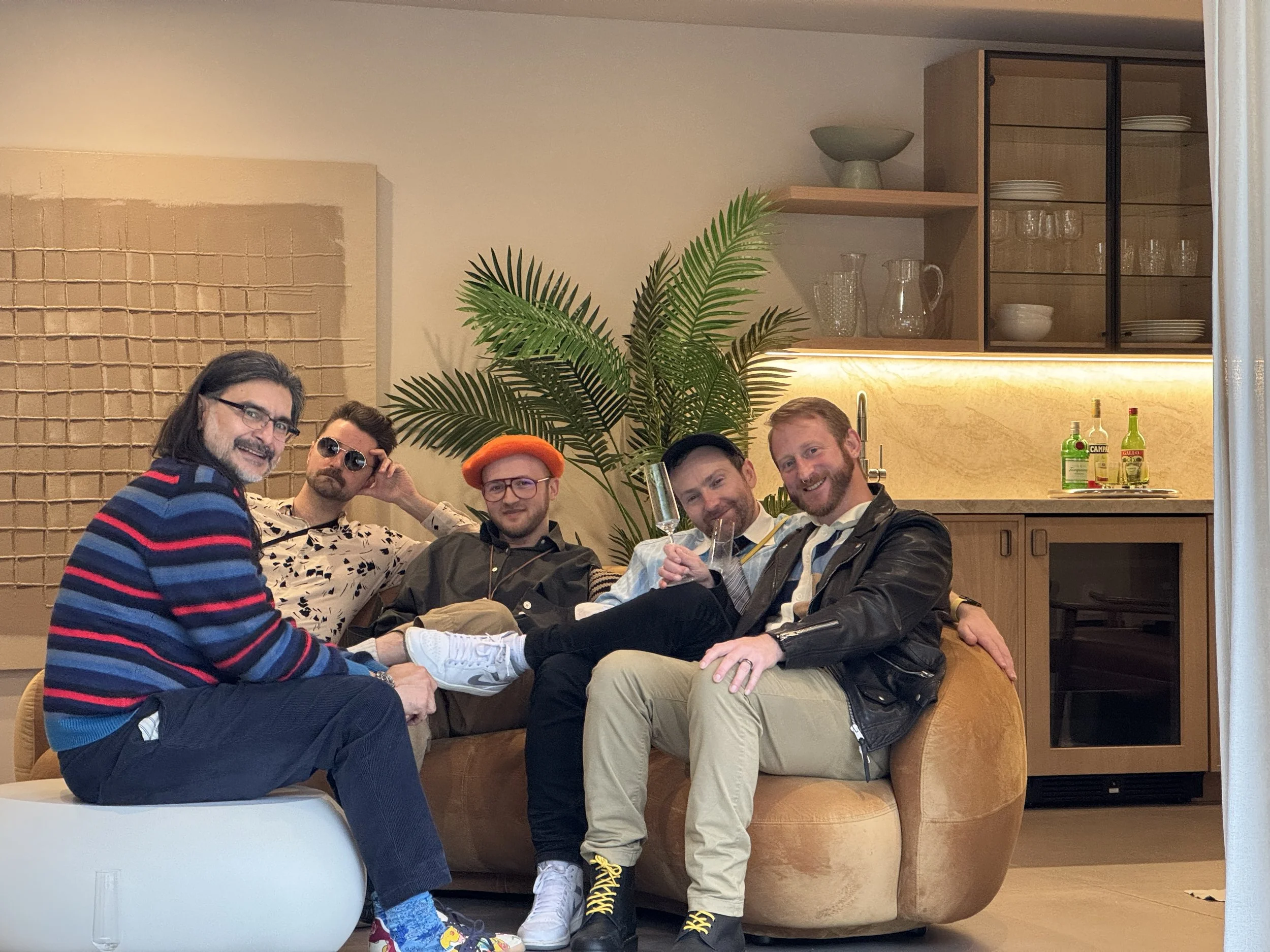People sitting on a suede couch in gorgeous outfits, smiling at the camera
