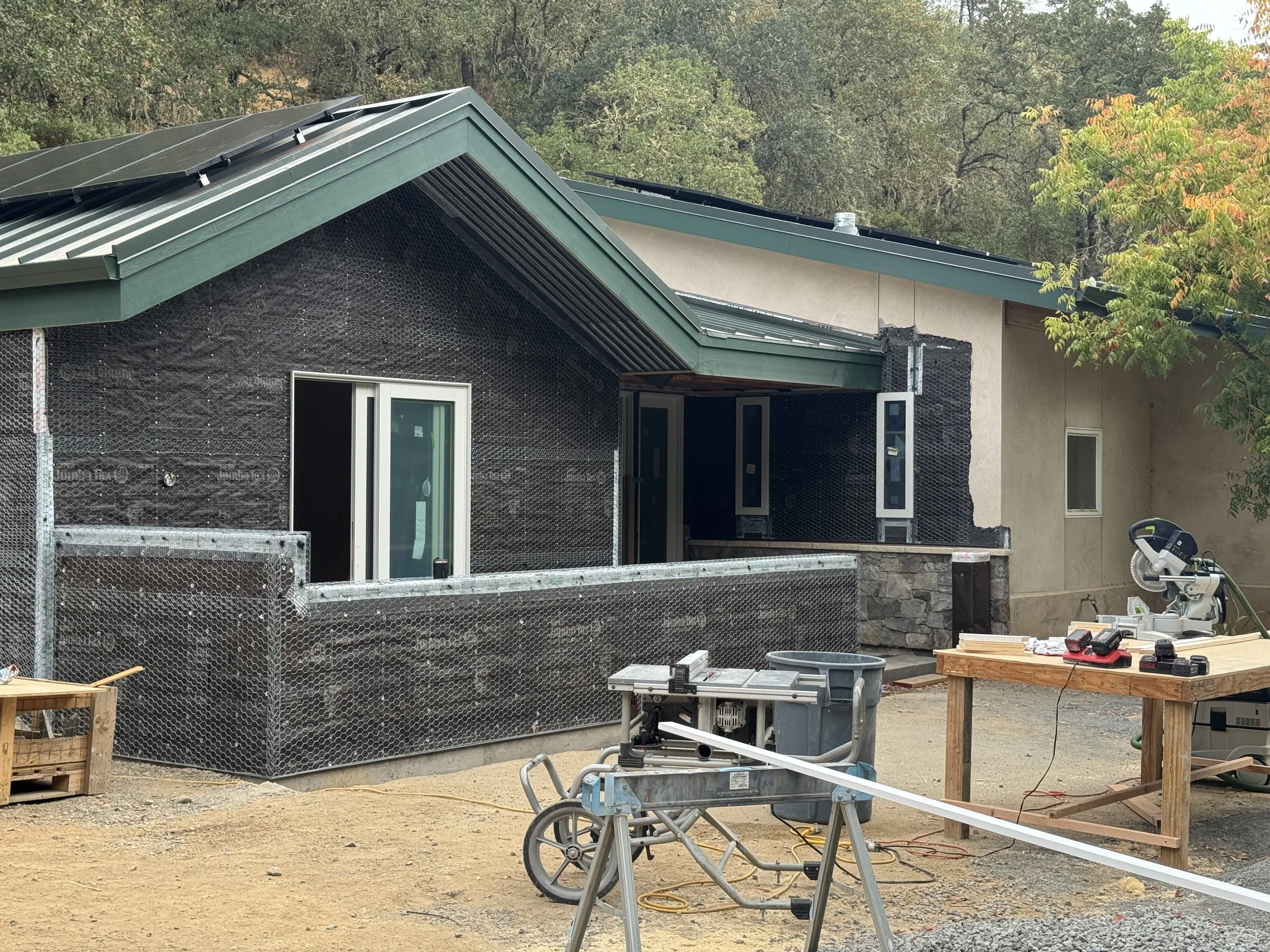 An exterior of the house addition under construction, the walls prepared to accept new stucco siding. Power tools in the foreground.