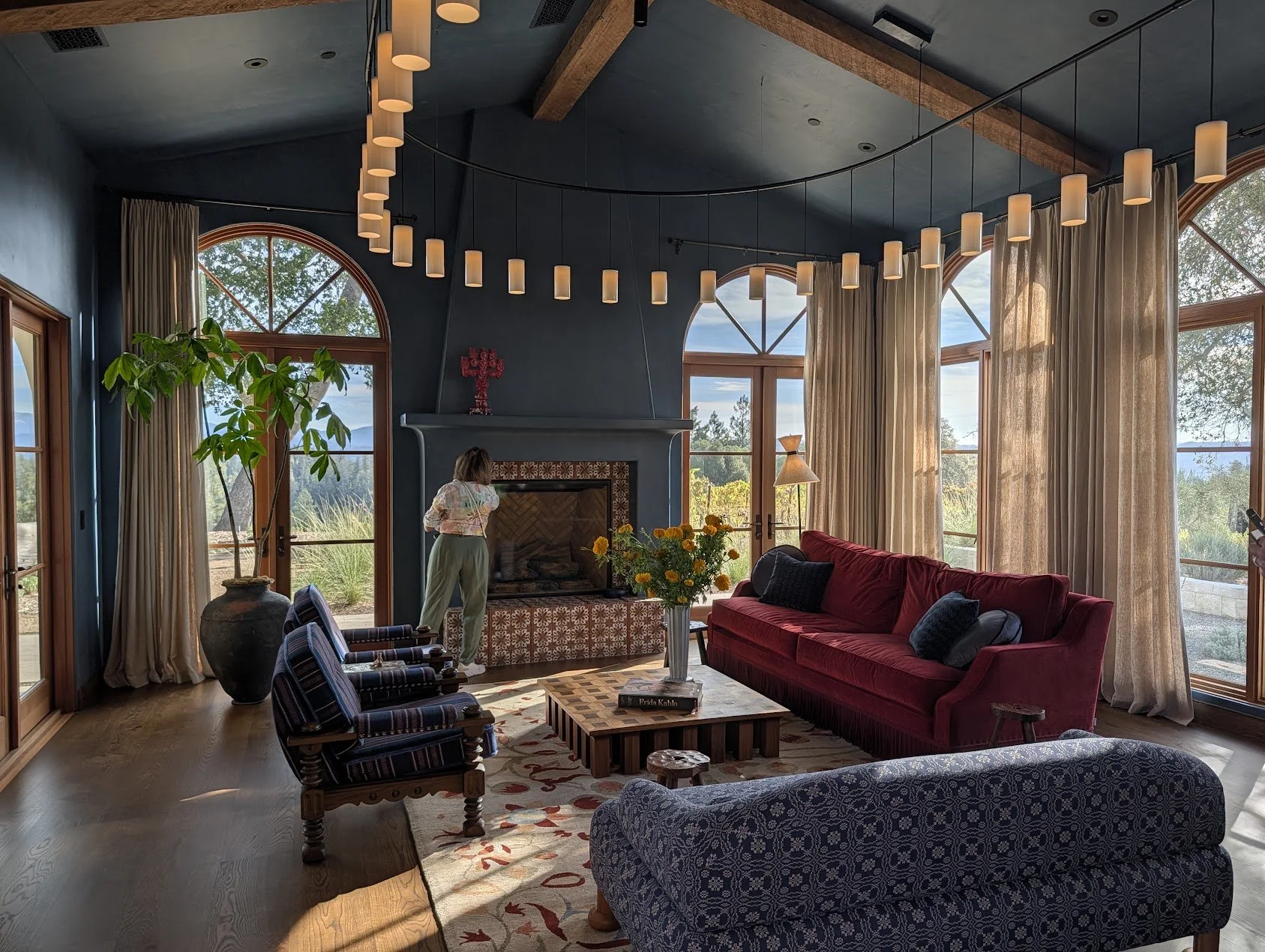 A living room with desaturated dark blue walls and a decorative tiled fireplace. A circuit of continuous pendant lights hangs over the space.