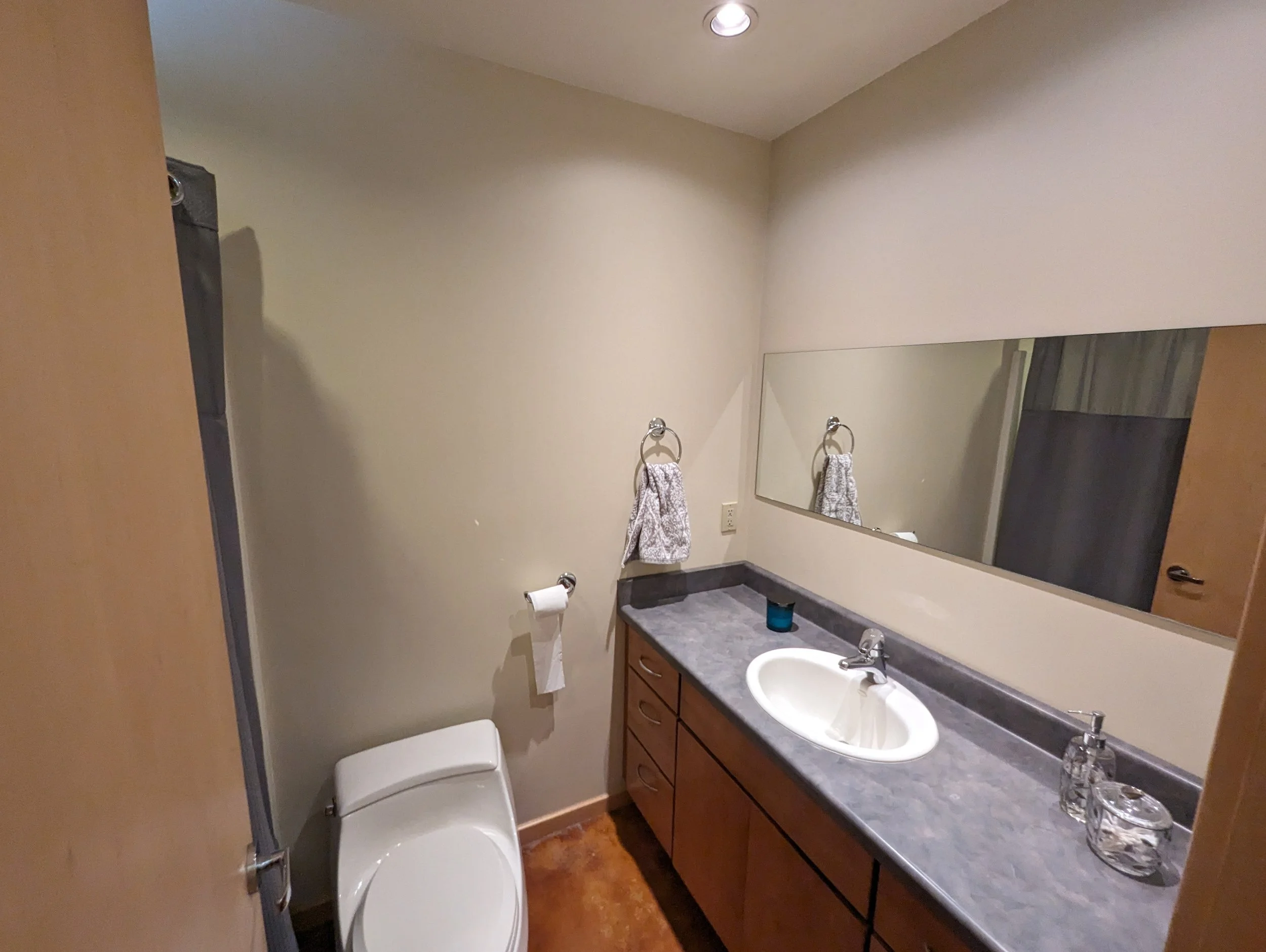 The old bathroom with orange floors and cabinets, a blue formica counter and horizontal wall mirror.
