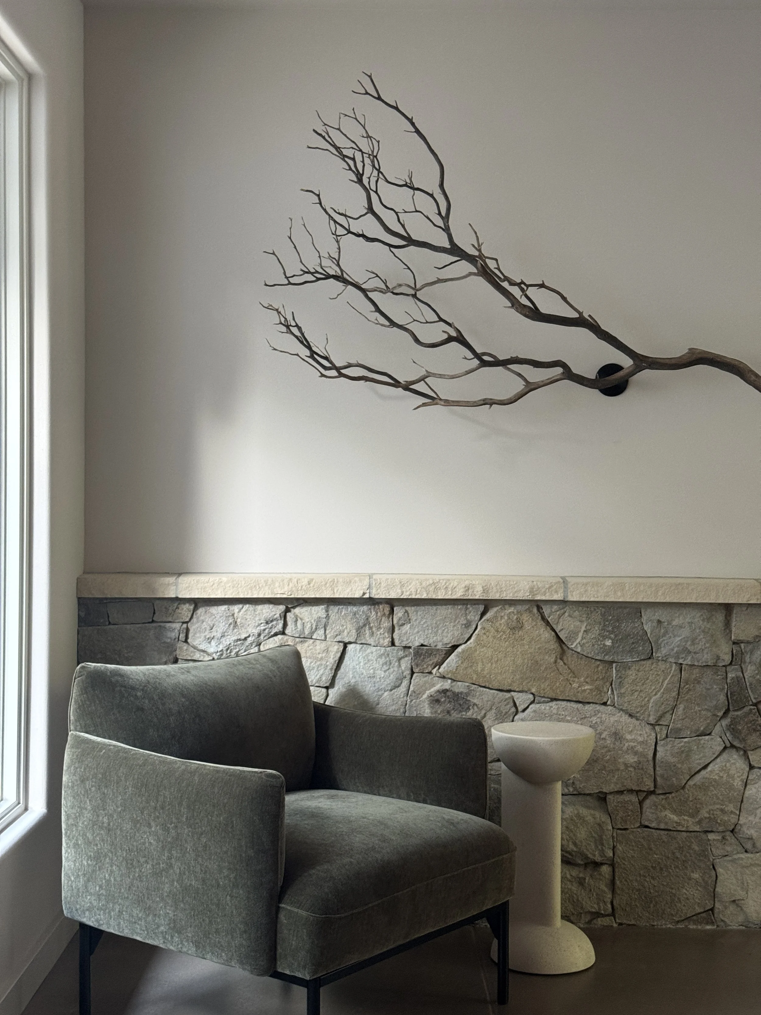 A green chair in front of a wall with stone wainscoting, a wall-mounted branch on the wall above the chair.