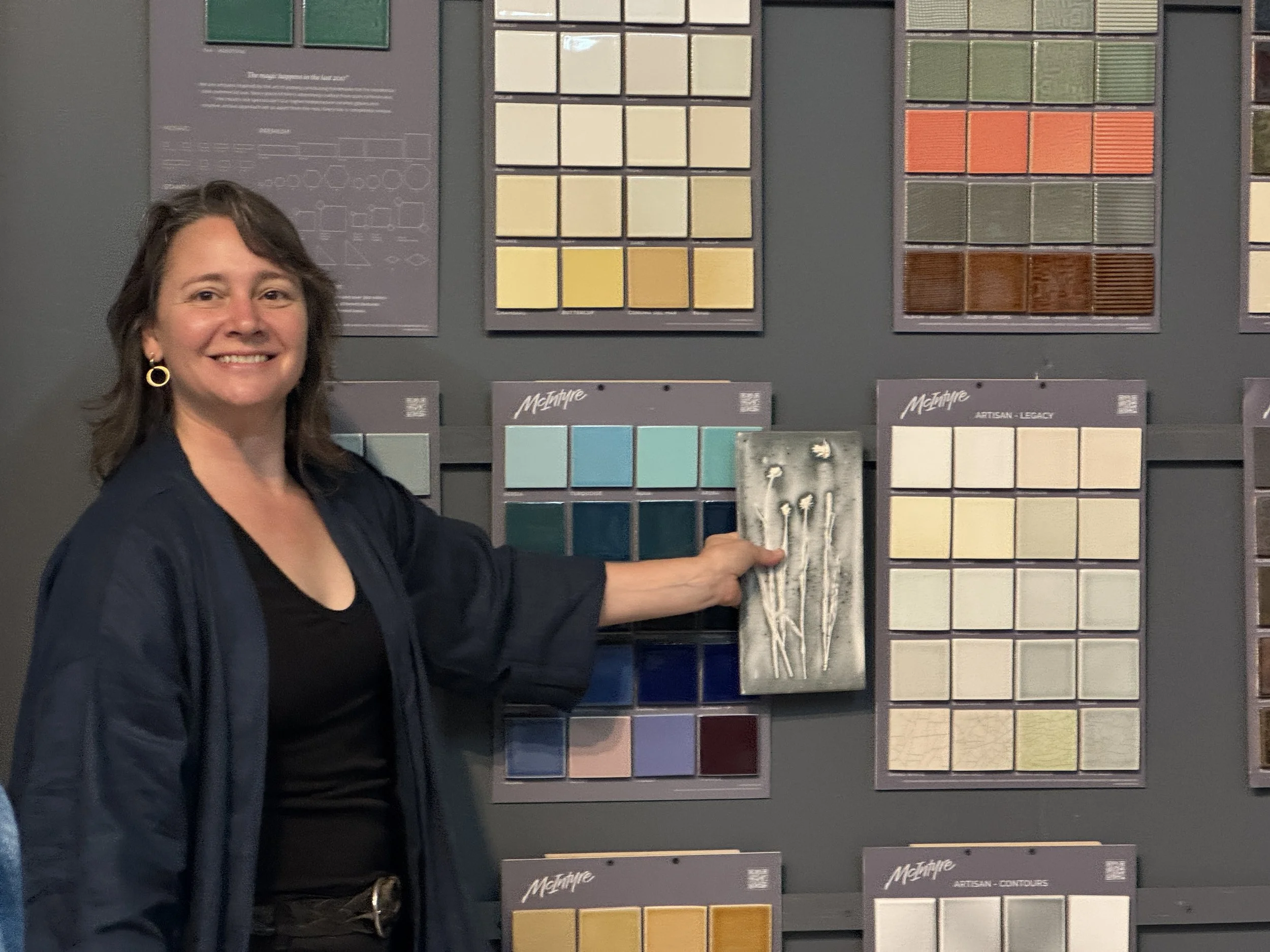The ceramic artist Kala Stein holding one of her tiles up against a palette of stock tile colors.