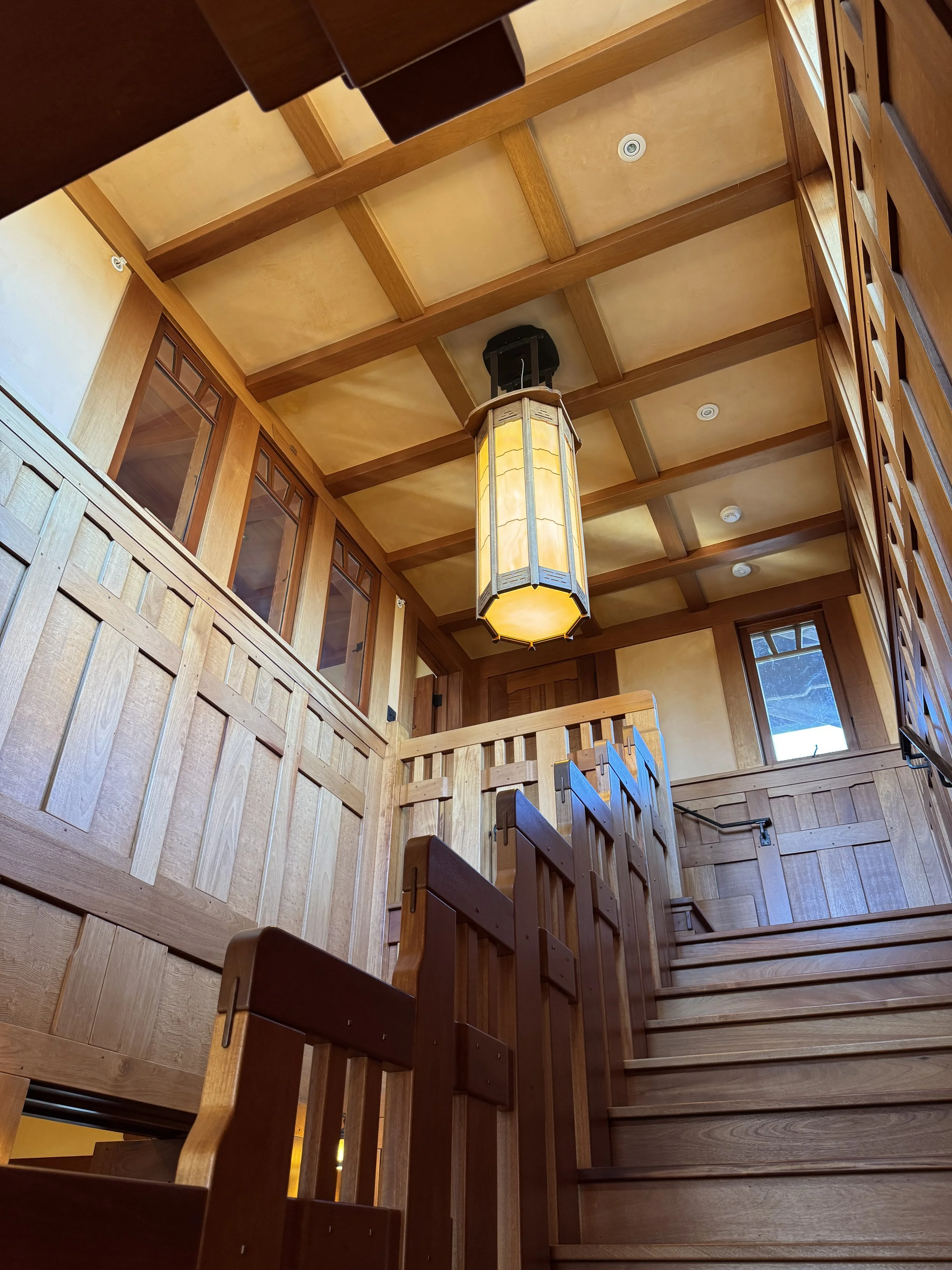 A wooden staircase with a mortice & tenon fabricated guardrail. A bespoke wooden pendant light hangs overhead.