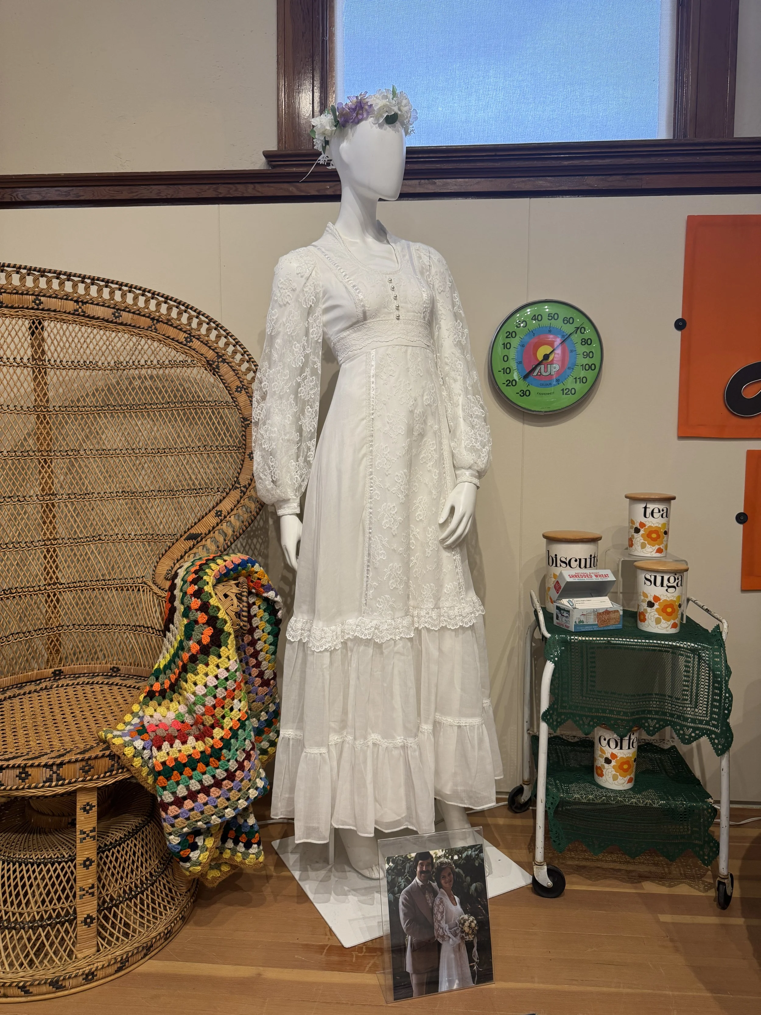 A museum display showing various 1970's products, including a white wedding dress.
