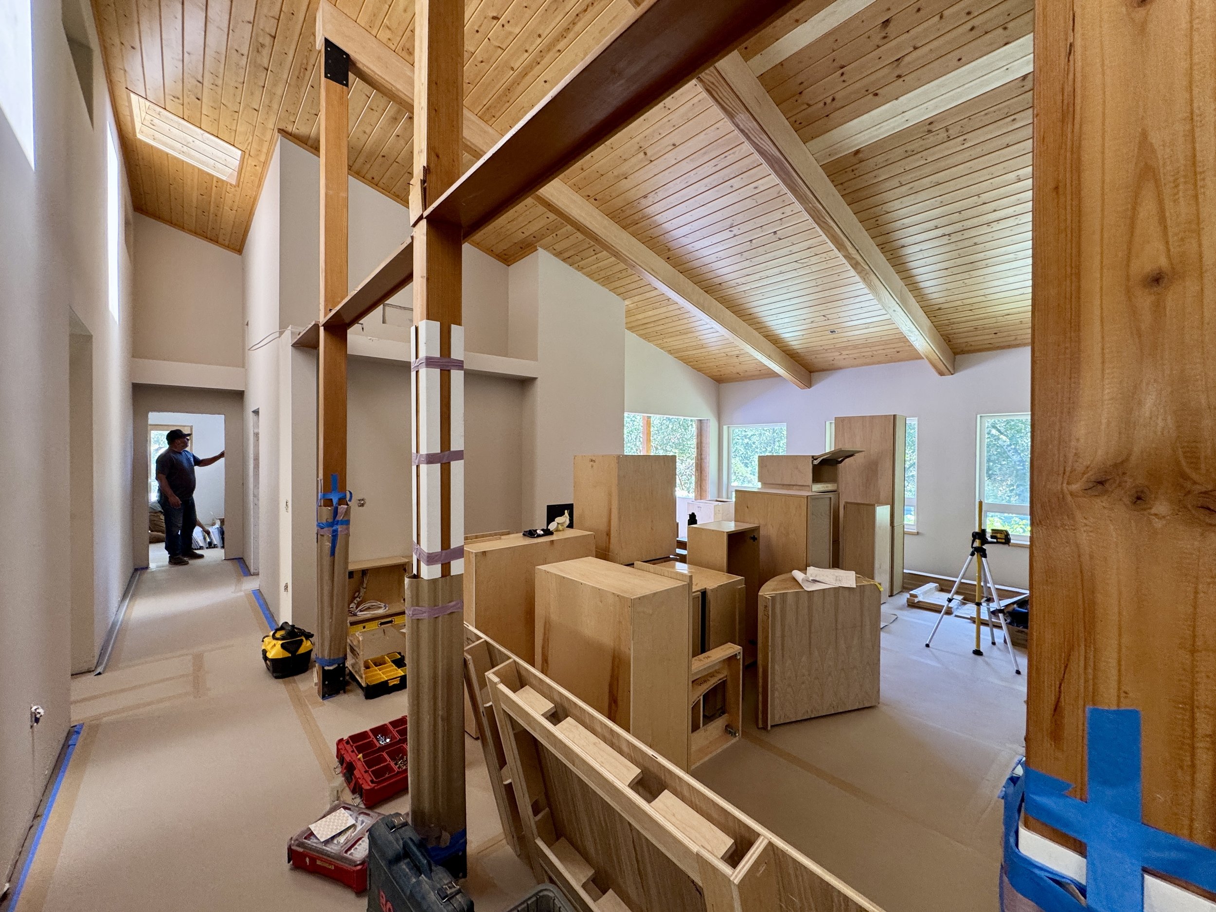 A large room with protective material on the walls and floors. Cabinetry not yet installed is stacked in the middle of the room with tools on the floor around them.