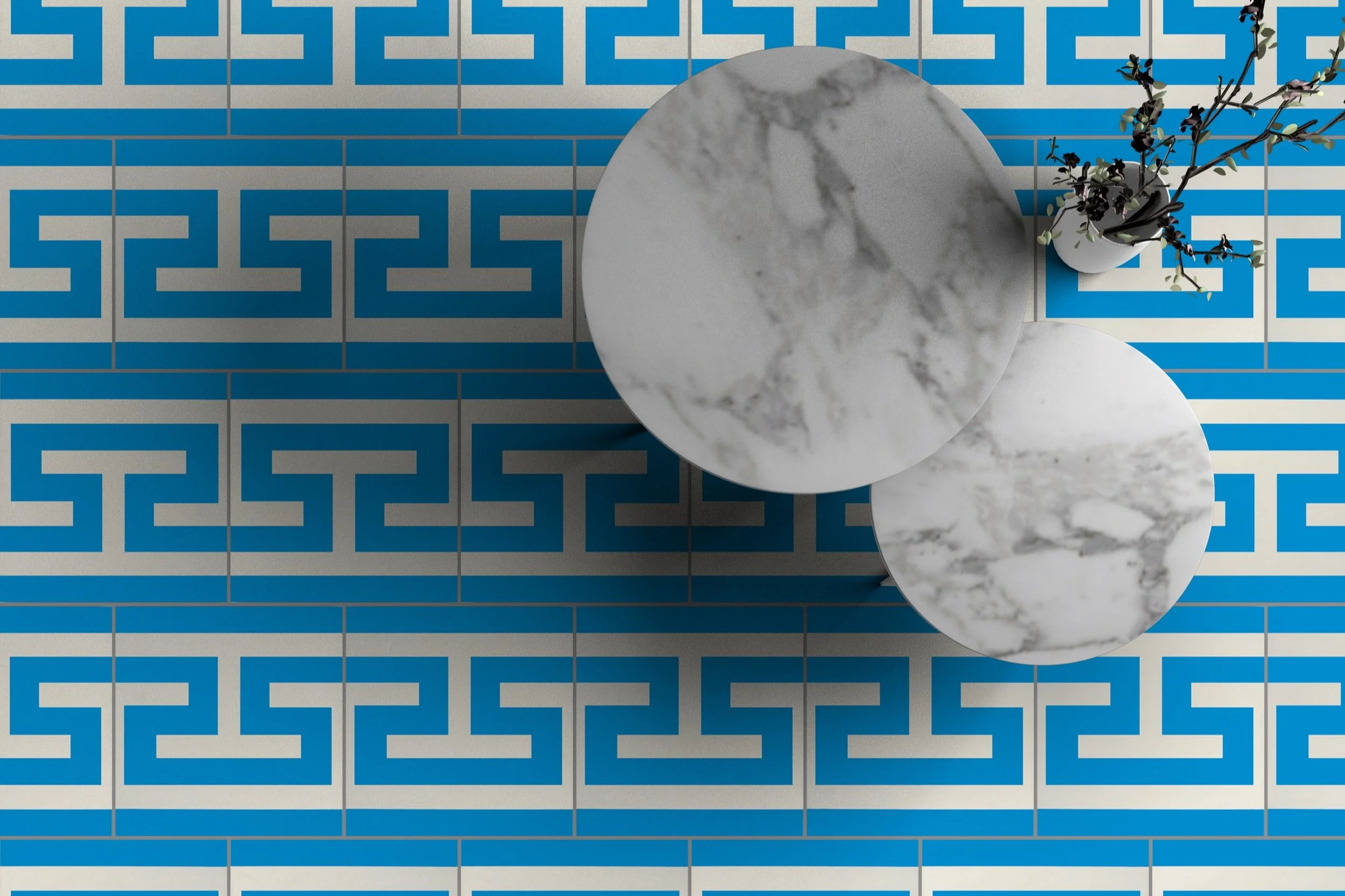 A top-down view of a room with blue and white patterned tiled floor, two round white marble tables, and a white vase with purple and green plant on the floor.