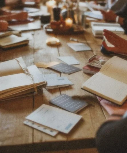 Ein Tisch mit geordneten und ungeordneten Büchern, Notizen und einigen kleinen Objekten, vermutlich in einer Bibliothek oder einem Arbeitsraum.