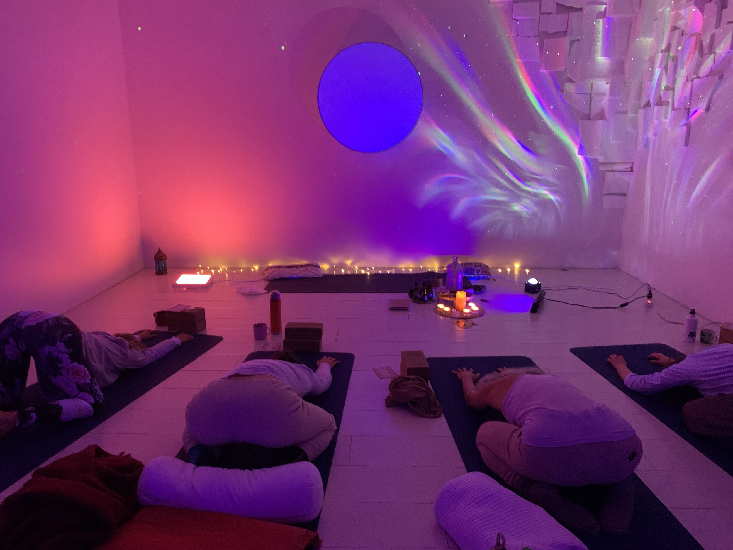 Menschen machen Yoga in einem stimmungsvoll beleuchteten Raum mit Kerzen und Lichteffekten an der Wand.