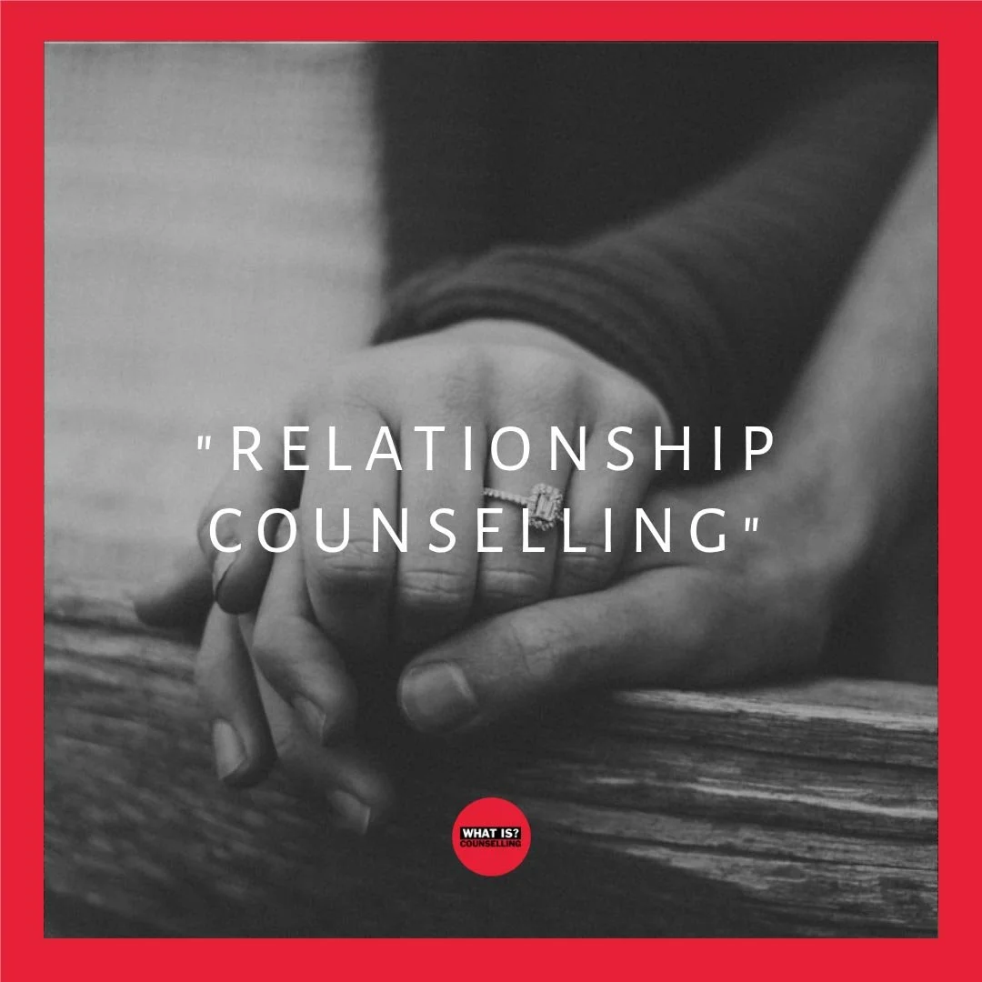 A black and white image showing two people holding hands and resting on some wood. One hand is wearing a ring