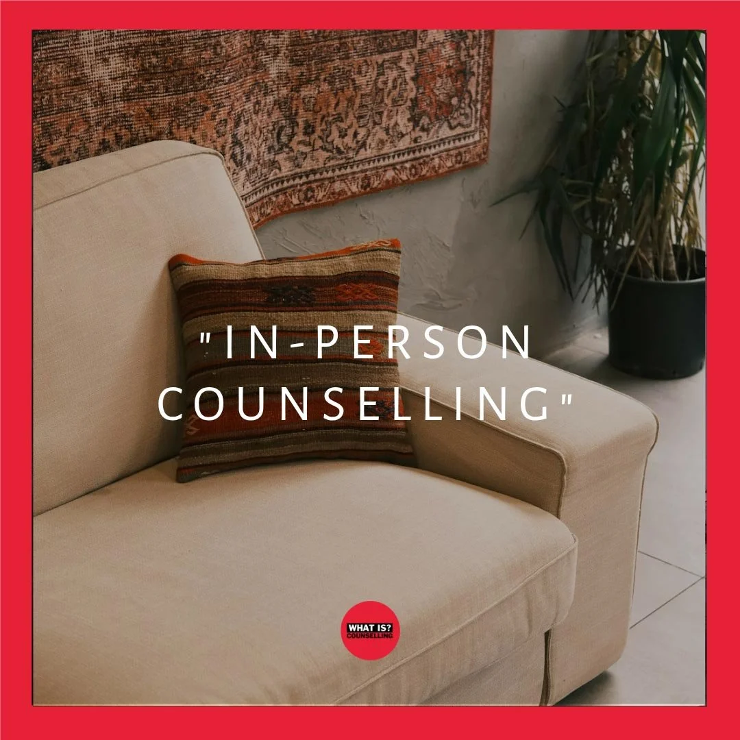An image of a comfy looking couch with a patterned cushion in the corner. A rug and plant are visible in the background on a tiled floor