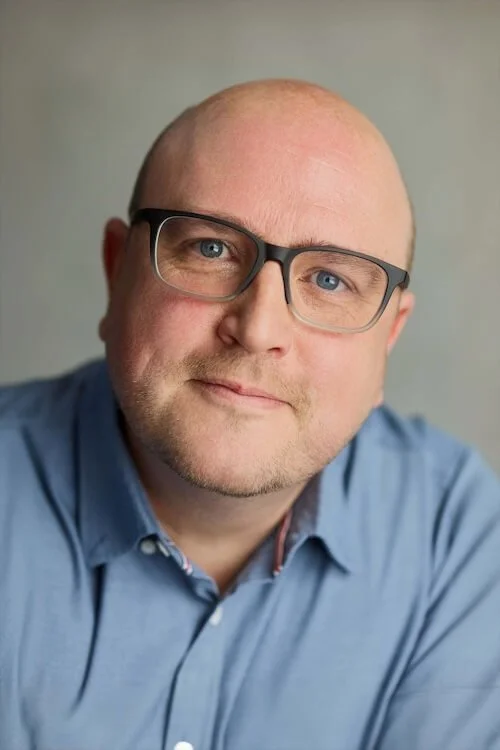 A portrait image of accredited counsellor James Pearson wearing a blue shirt and blue glasses
