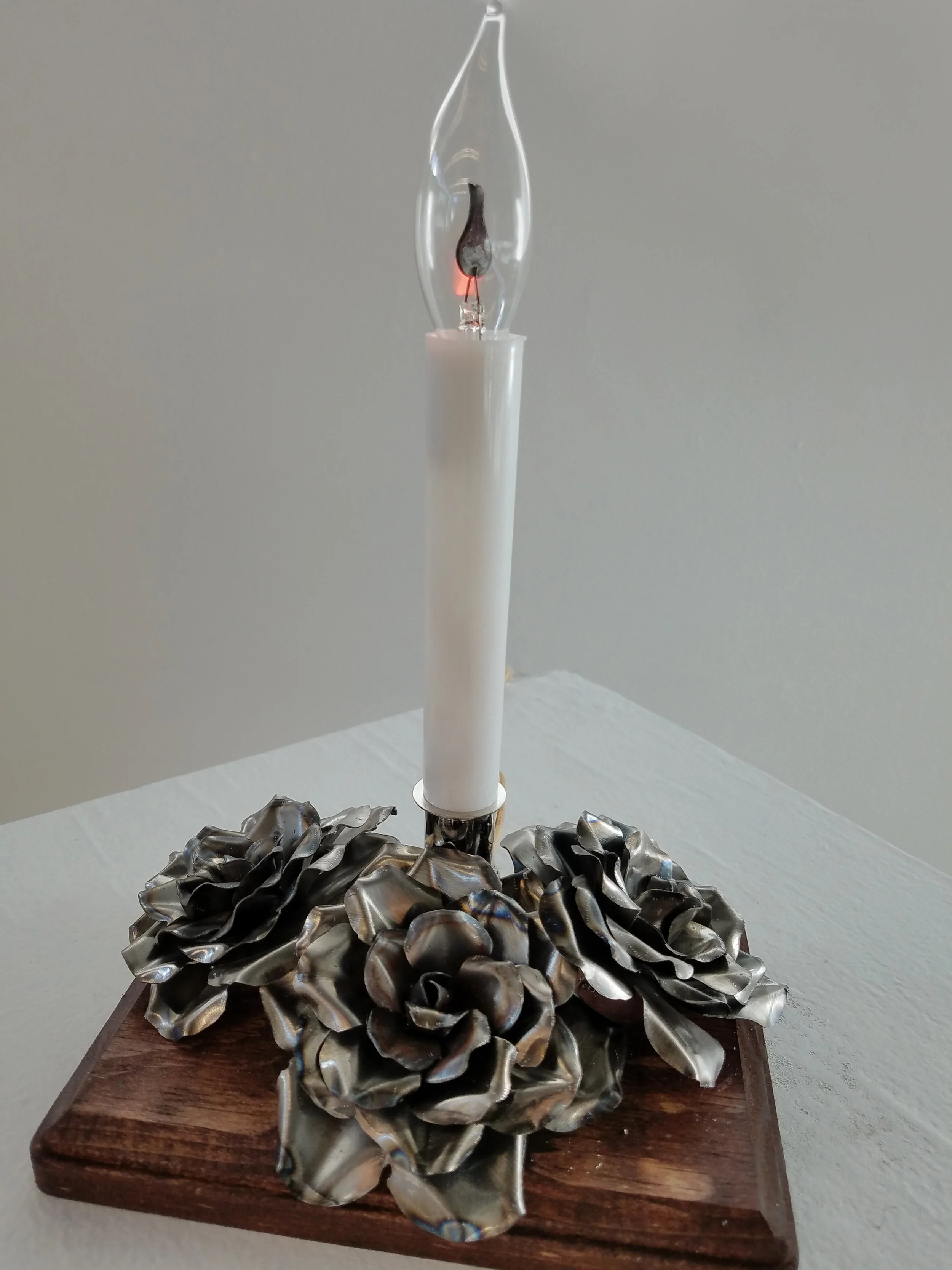 Electric candle with three metal roses mounted to a wooden base.