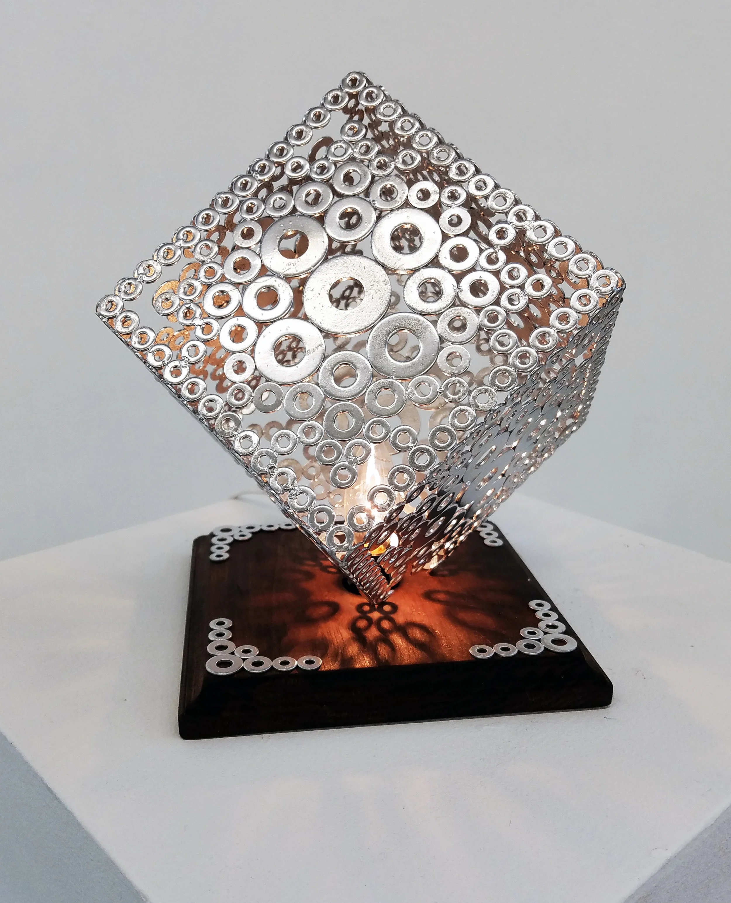 Cube shaped light made of o-rings mounted on wooden base.