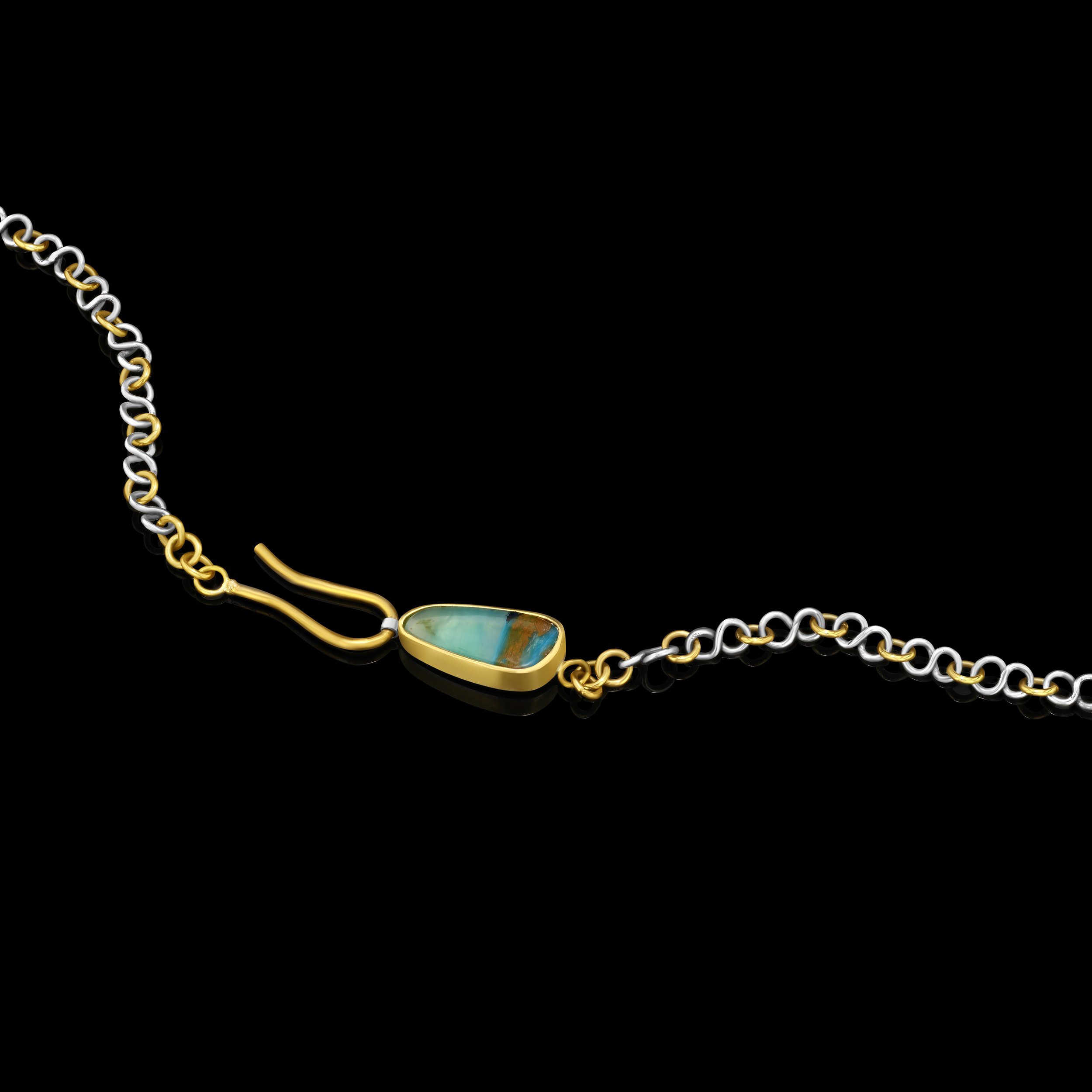 close up on clasp of bright blue stone on a necklace with alternating gold and silver links