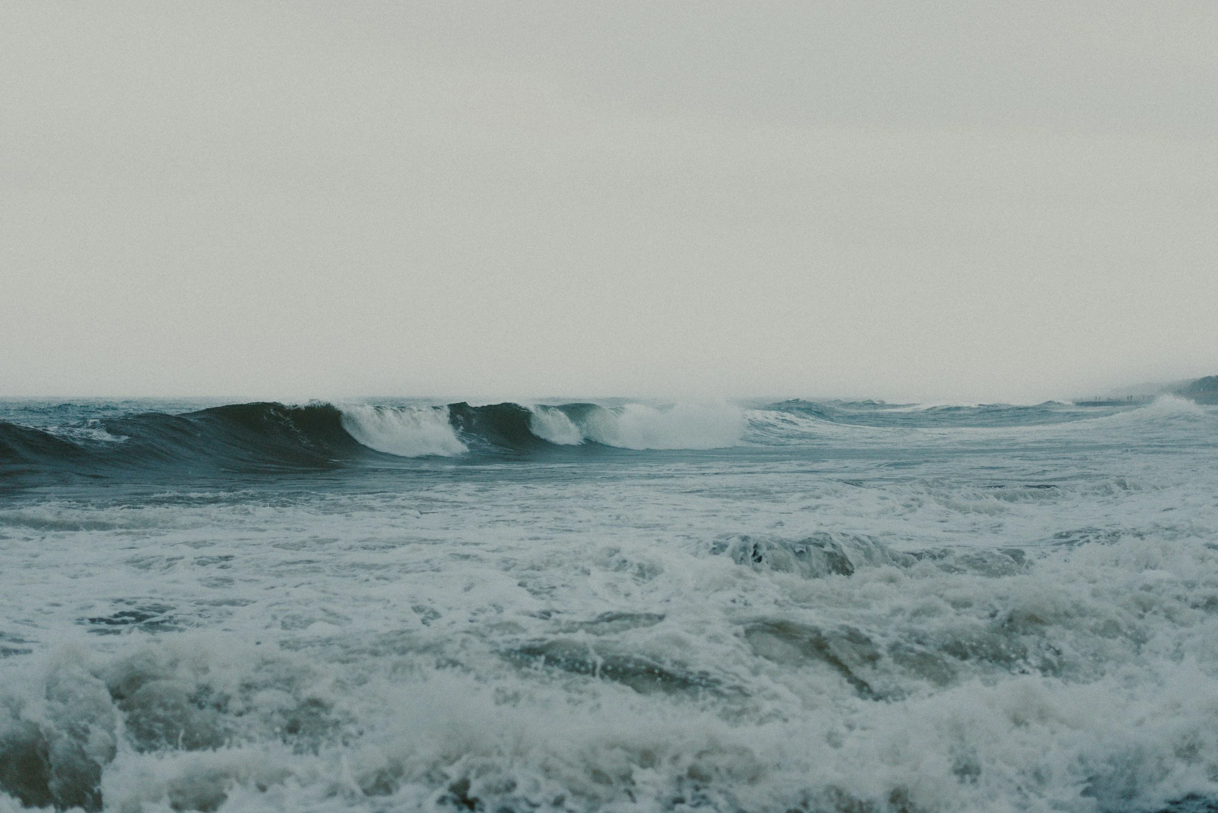 Ocean waves crashing on the shore with a cloudy sky.