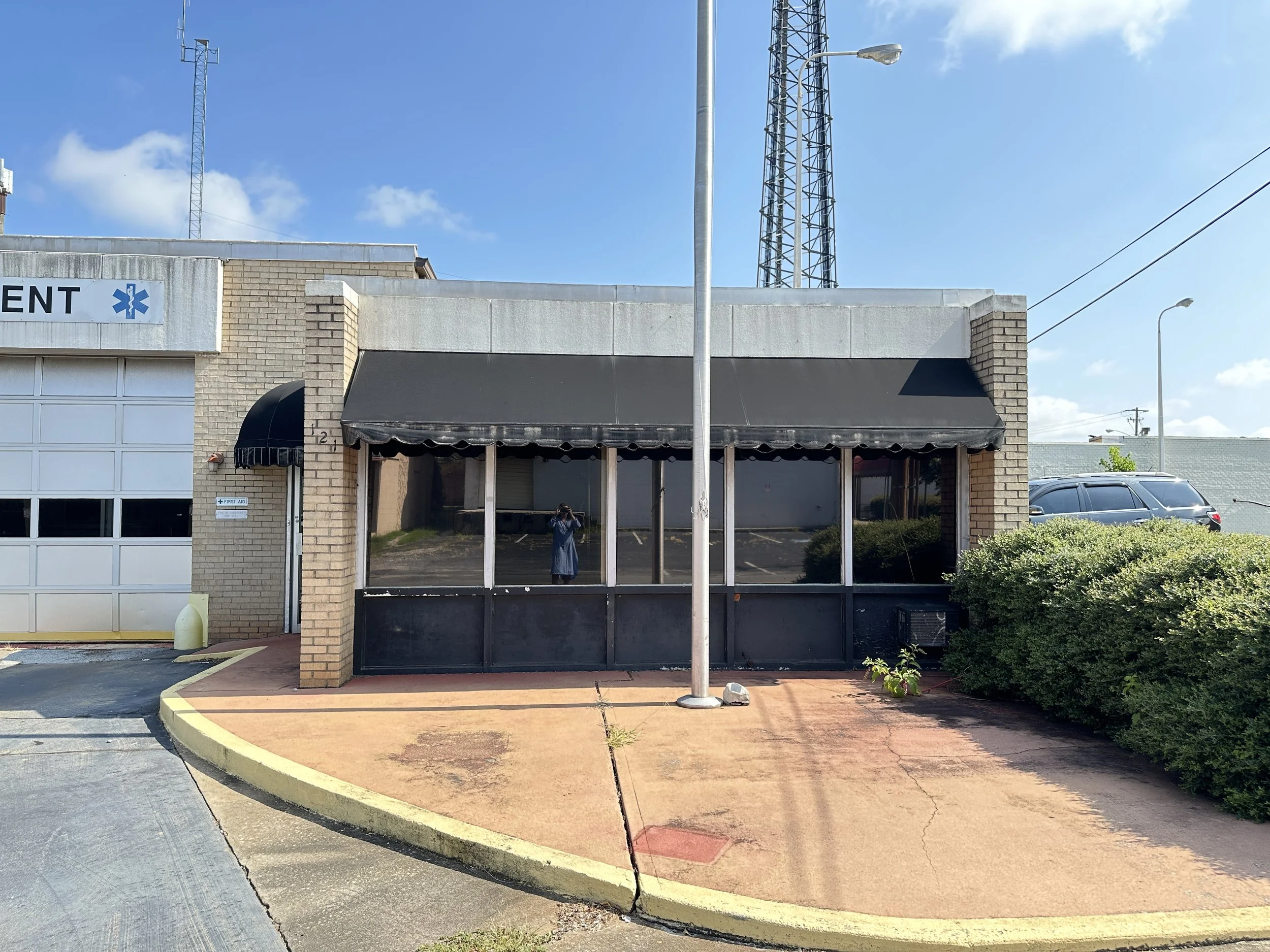 Front view of a building with a black awning and a glass door, surrounded by parking lot and street signs, with blue sky and antennas on top