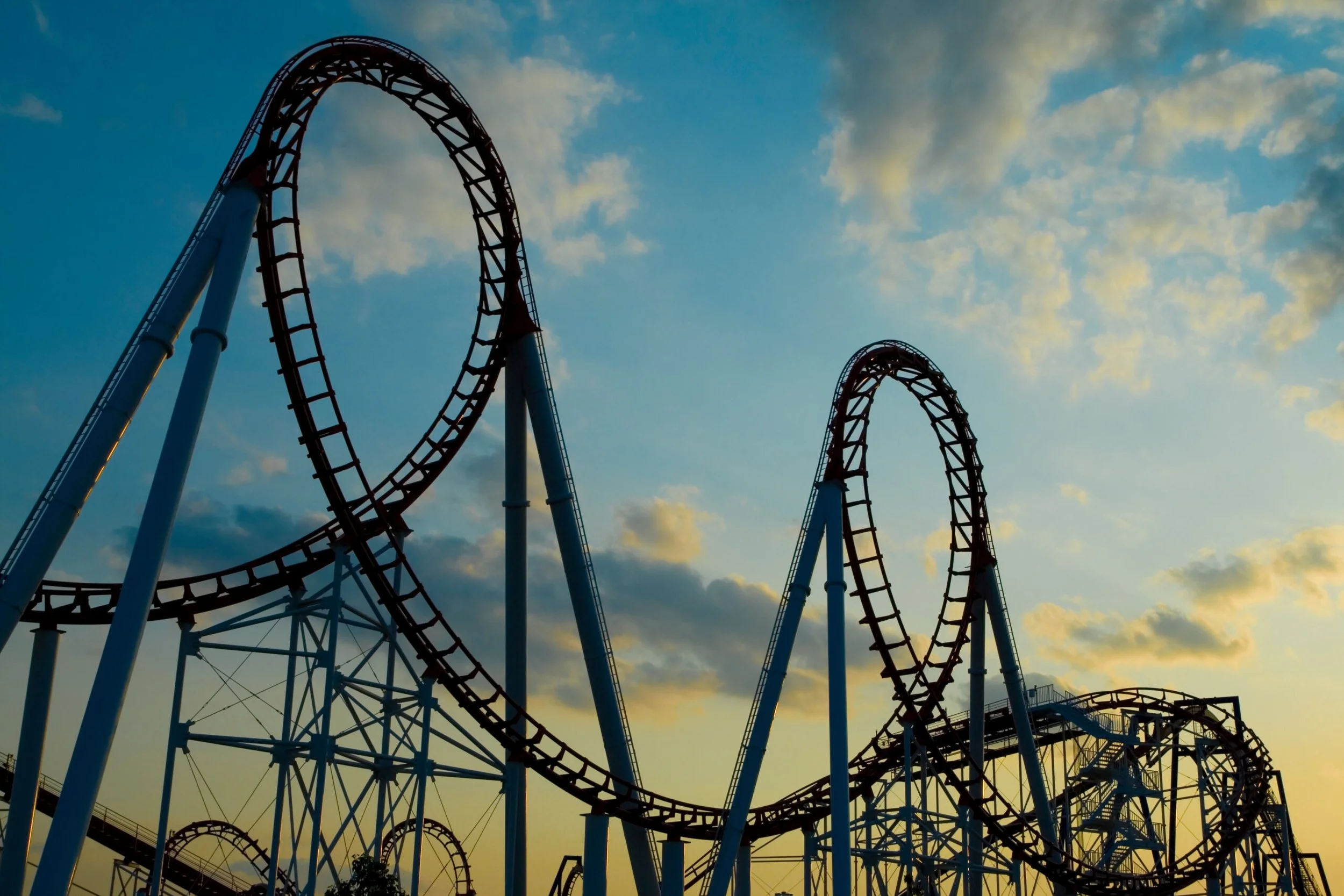 A roller coaster ride at an amusement park during sunset, with looping tracks against a partly cloudy sky.