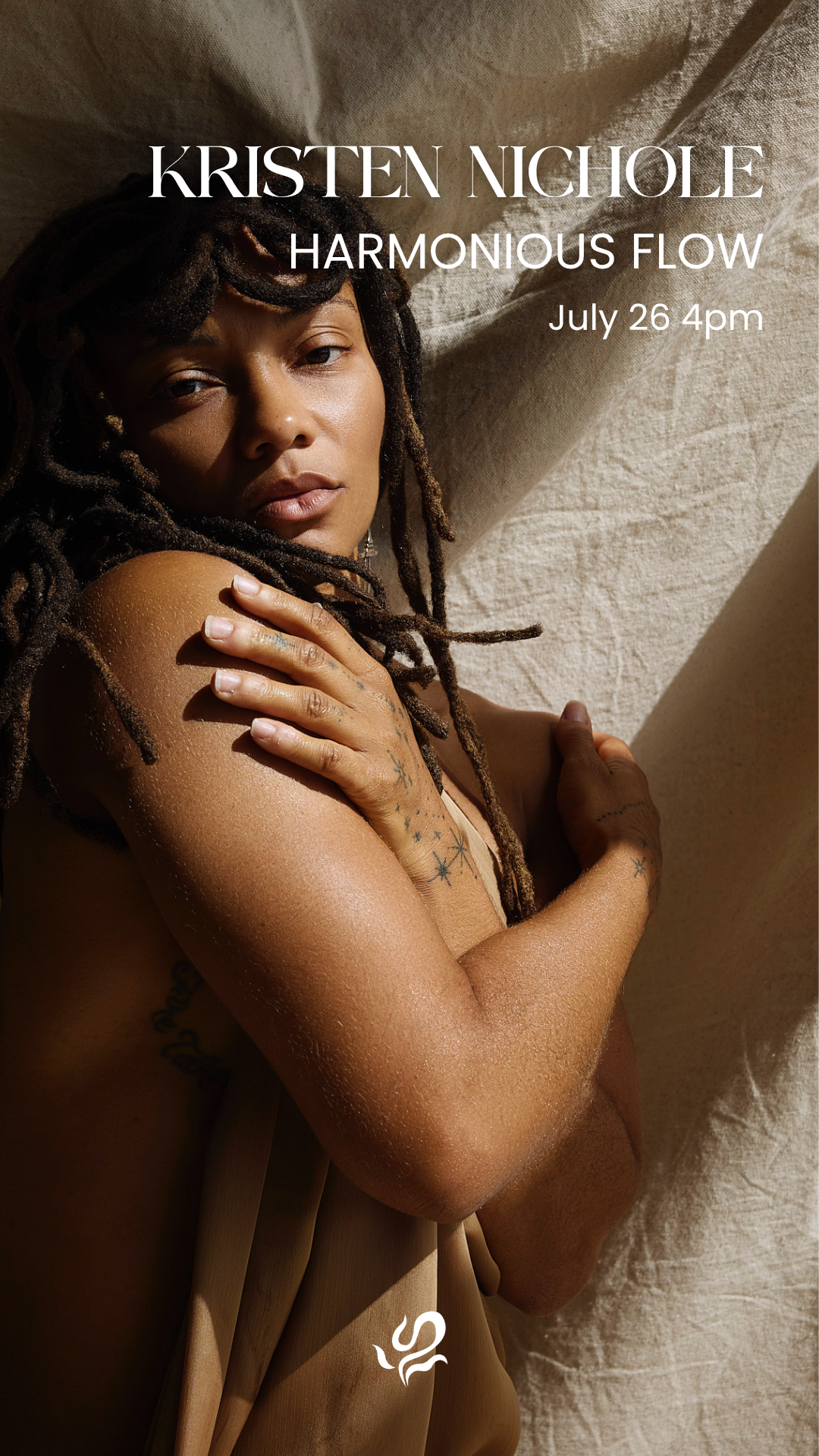 A woman with tattoos on her arm and hand, lying on a fabric surface. She is looking directly at the camera with a relaxed expression.