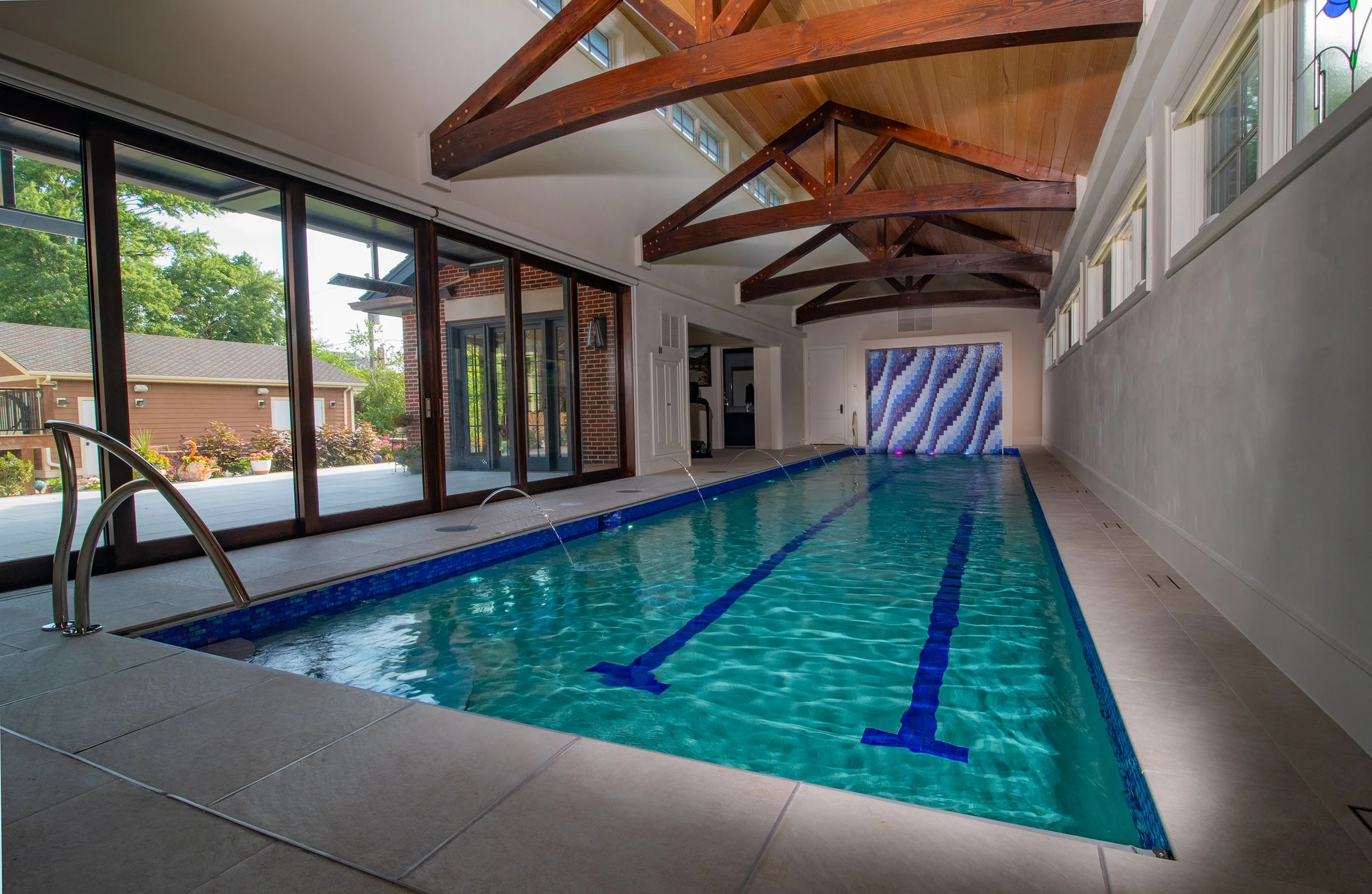Residential Indoor lap pool with mosaic tile water wall feature beautiful hardwood ceiling finishes stained glass built by Barrington Pools