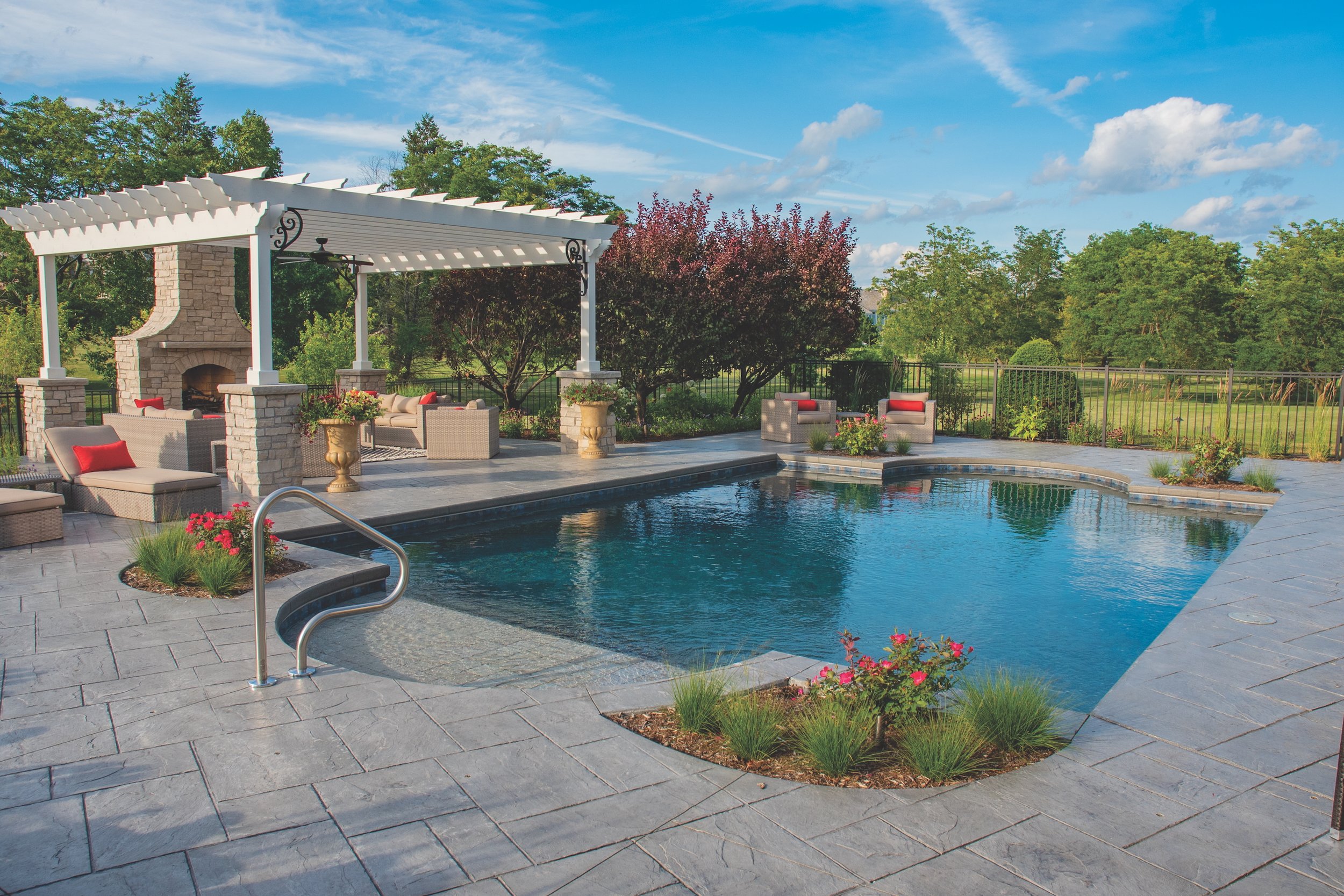 Backyard with a swimming pool, pergola, and outdoor seating area, surrounded by landscaped gardens and trees.