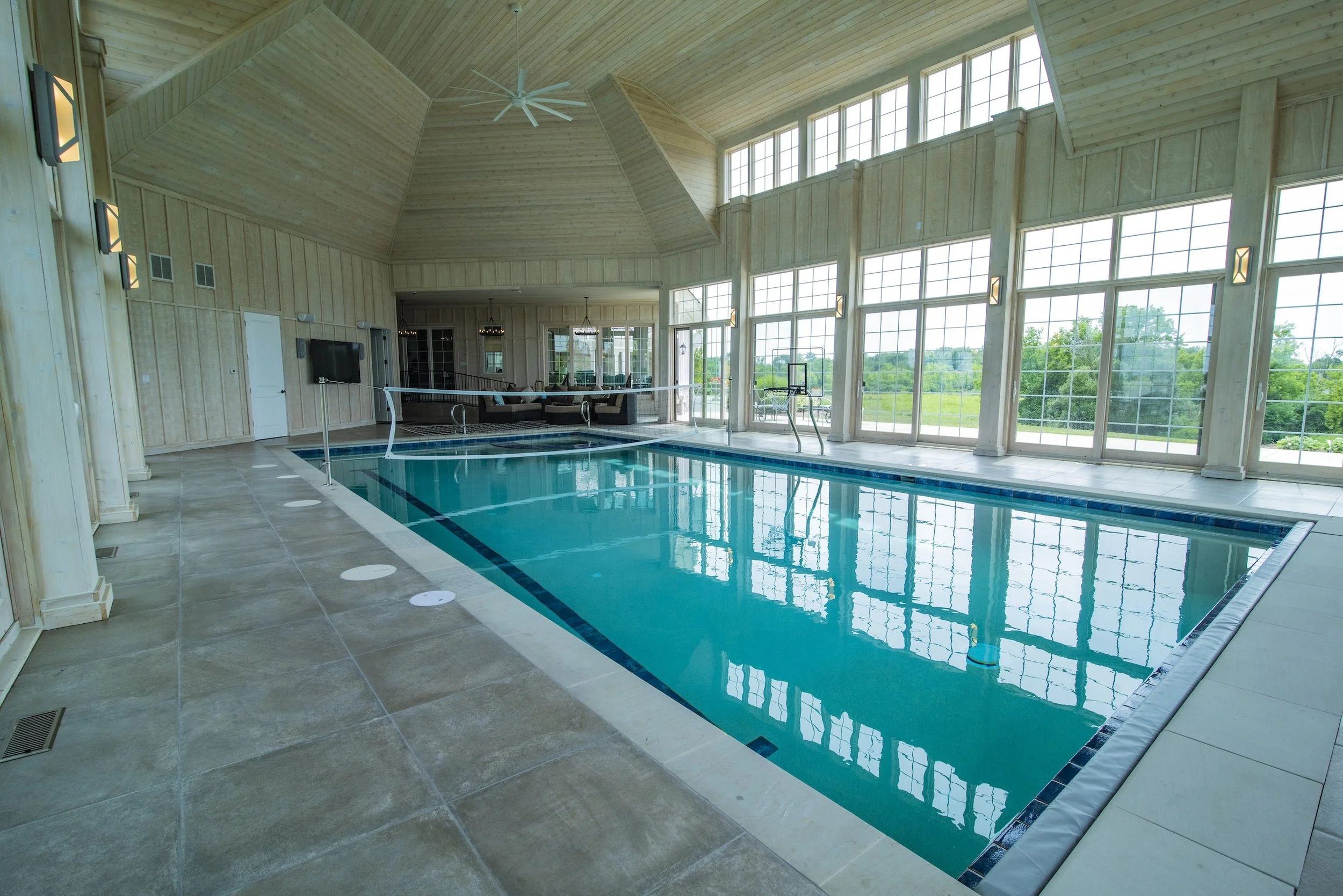 Indoor swimming pool with large windows, a high ceiling, pool deck, and surrounding lounge area.