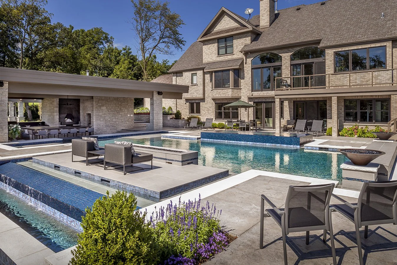 Luxury outdoor pool with modern patio and covered lounge area next to a large home.
