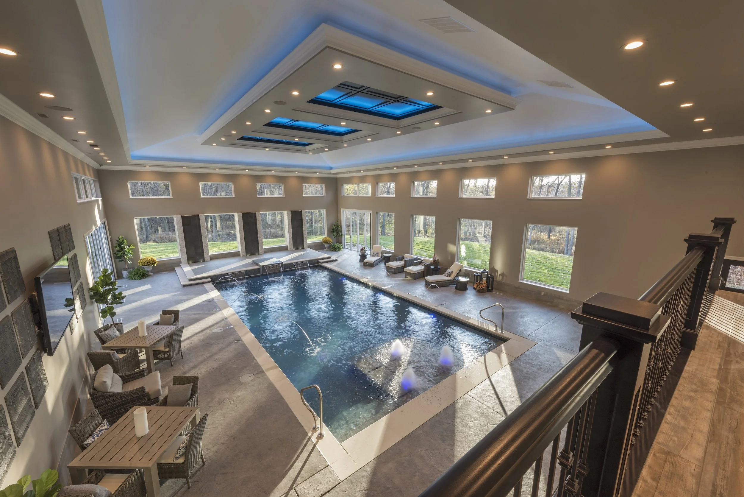Luxury indoor swimming pool with seating area, modern lighting, and large windows overlooking a garden.