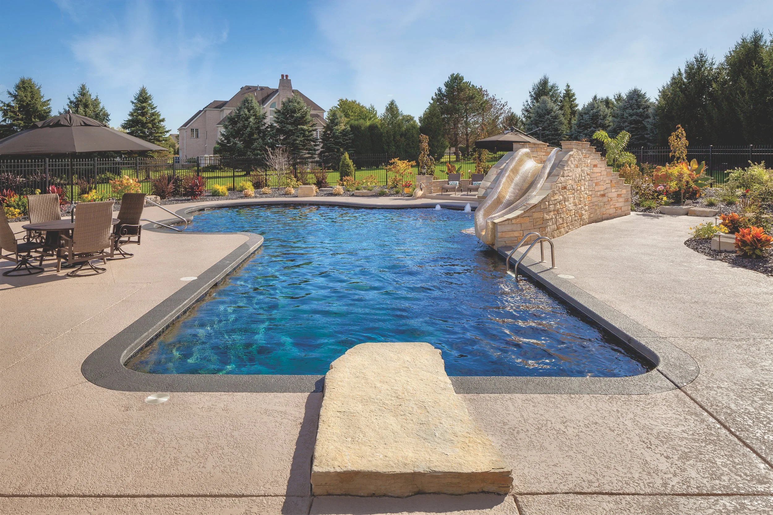 Backyard with swimming pool, slide, patio furniture, and garden landscaping.
