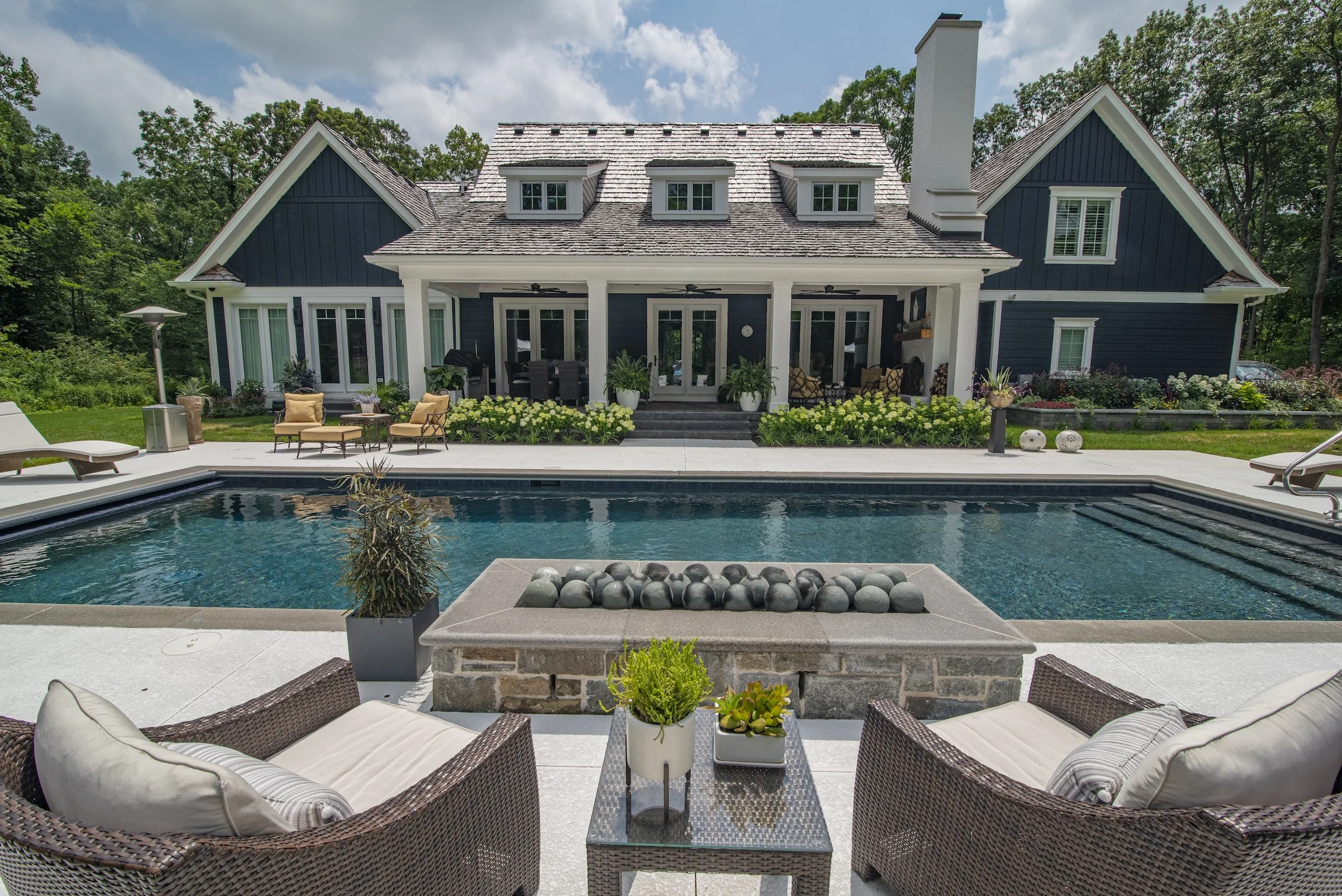 Luxury house with a swimming pool, patio furniture, landscaped garden, and lounge chairs; features a modern design with a stone pathway and a covered porch.