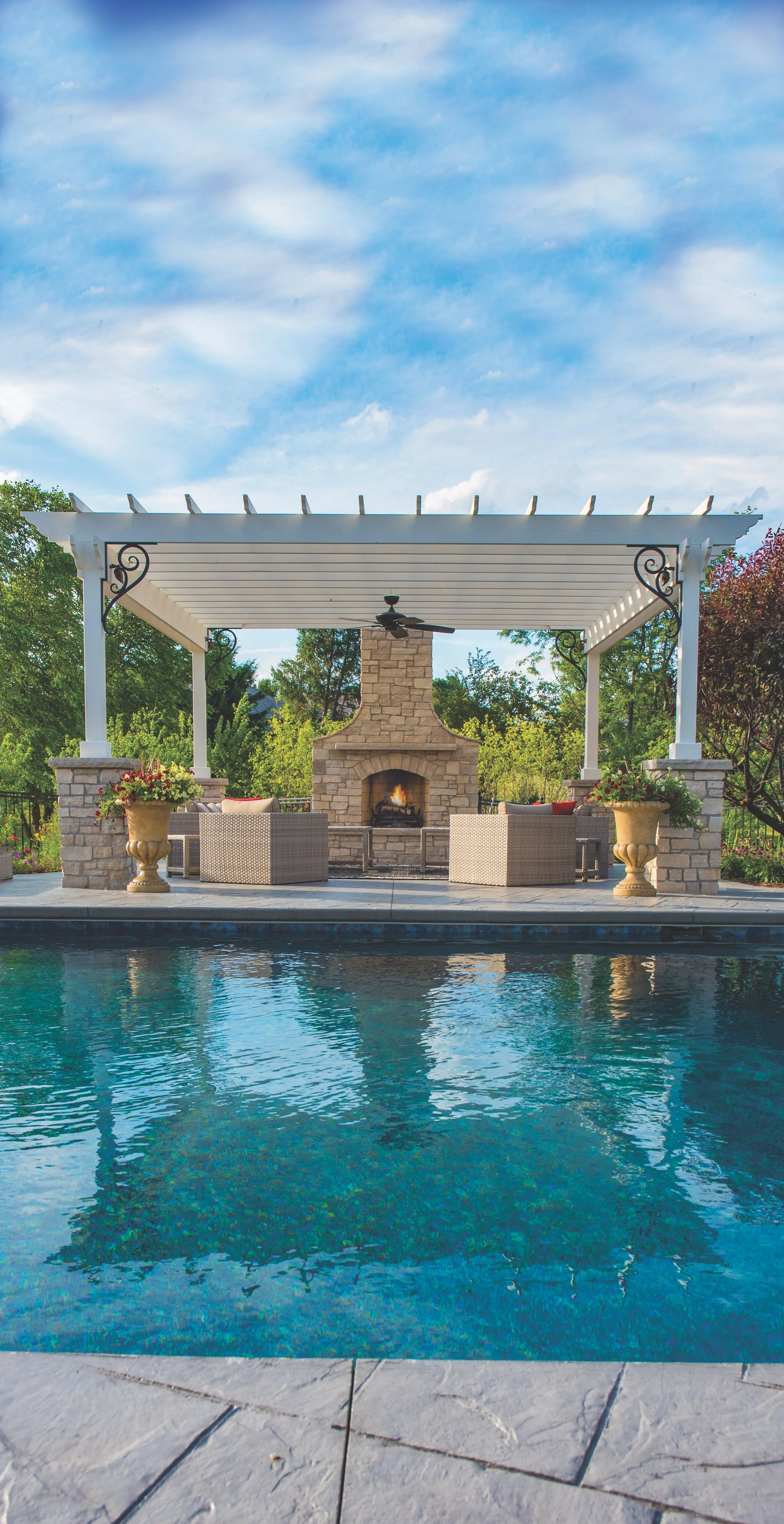 Backyard with a swimming pool, pergola, fireplace, and patio furniture beneath clear blue sky.