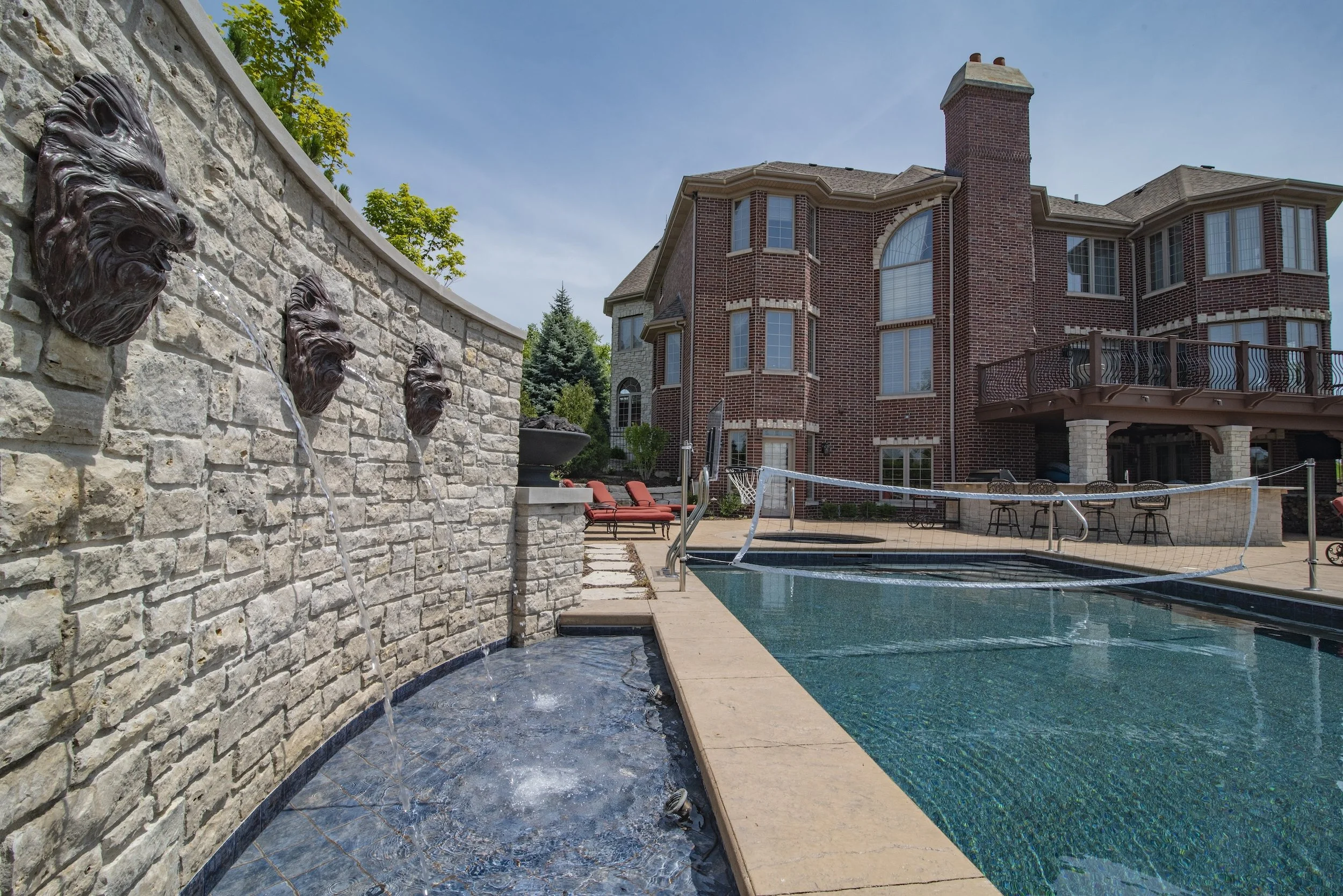 Luxury backyard with stone fountain and pool volleyball setup.