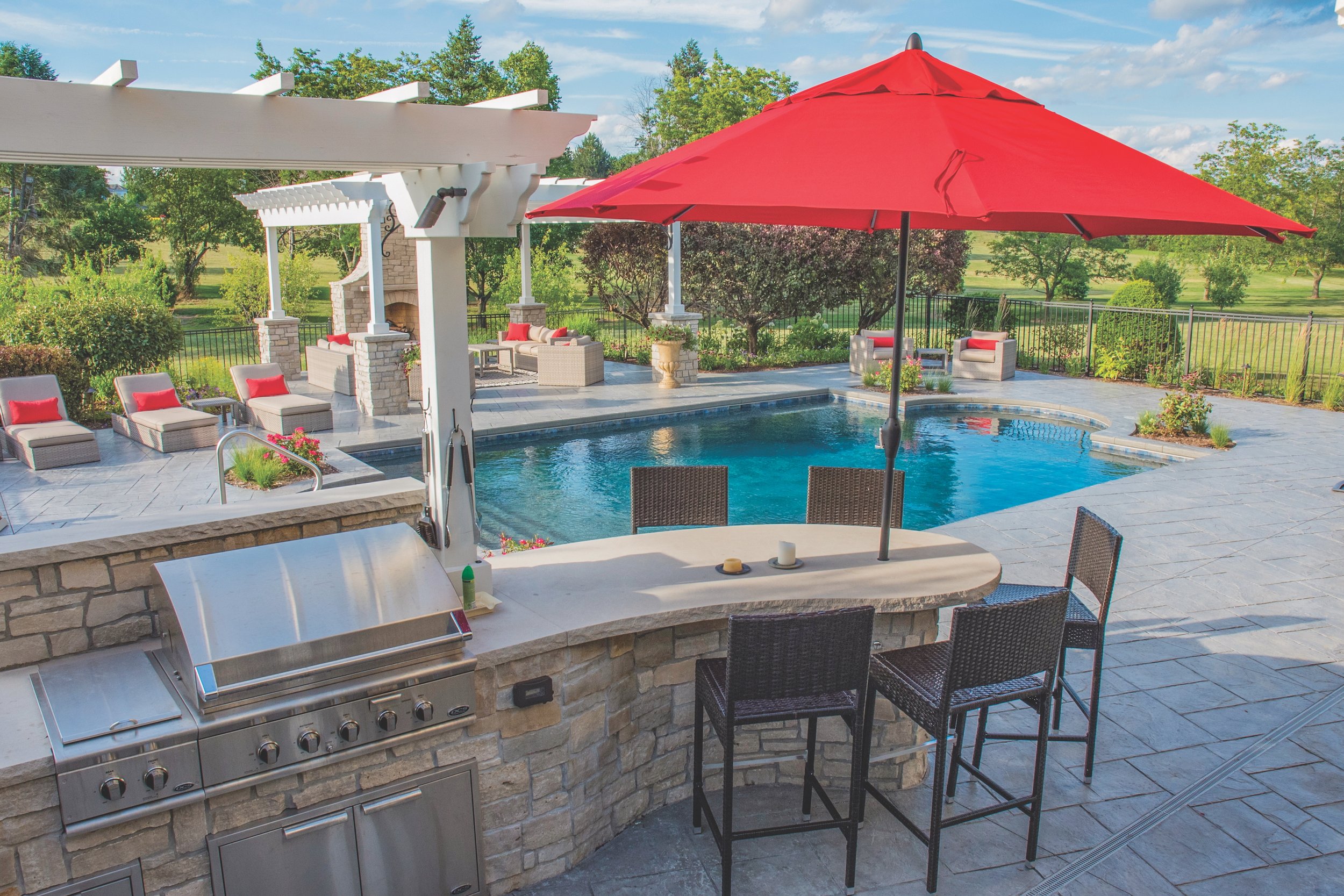 Backyard with a swimming pool, outdoor kitchen with a grill, patio furniture, and a large red umbrella.
