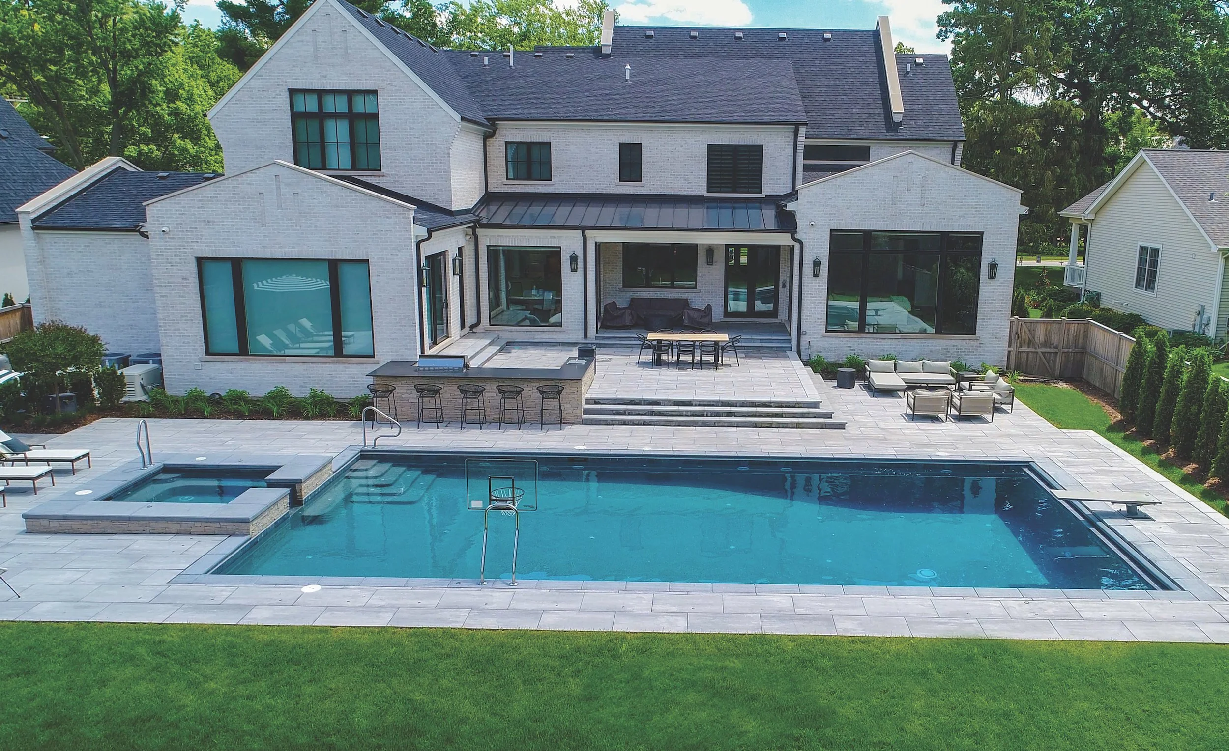 Elegant modern house with large swimming pool and patio in a landscaped backyard.