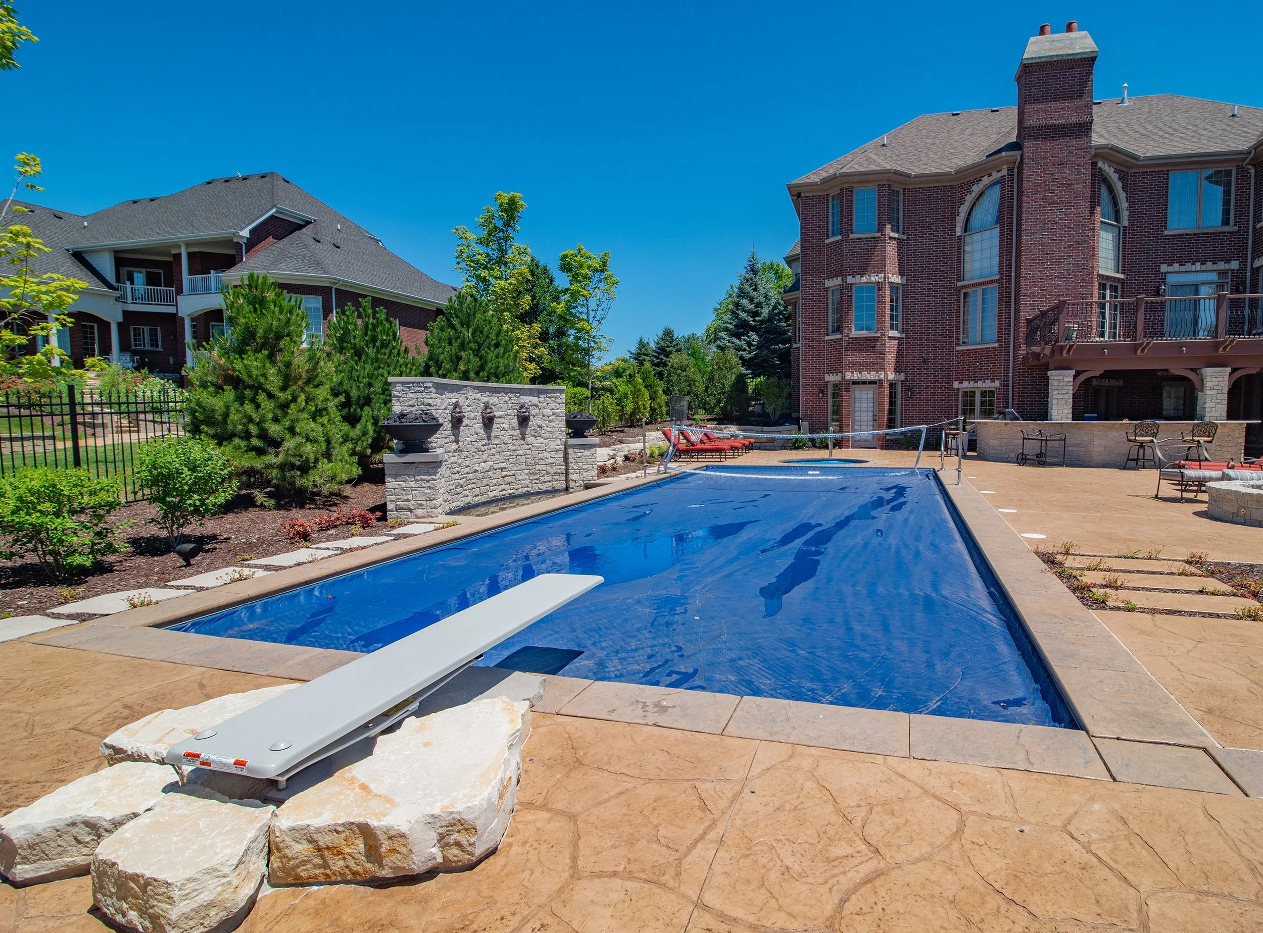 Luxury home with an outdoor swimming pool, diving board, and patio area, surrounded by landscaping and brick architecture.