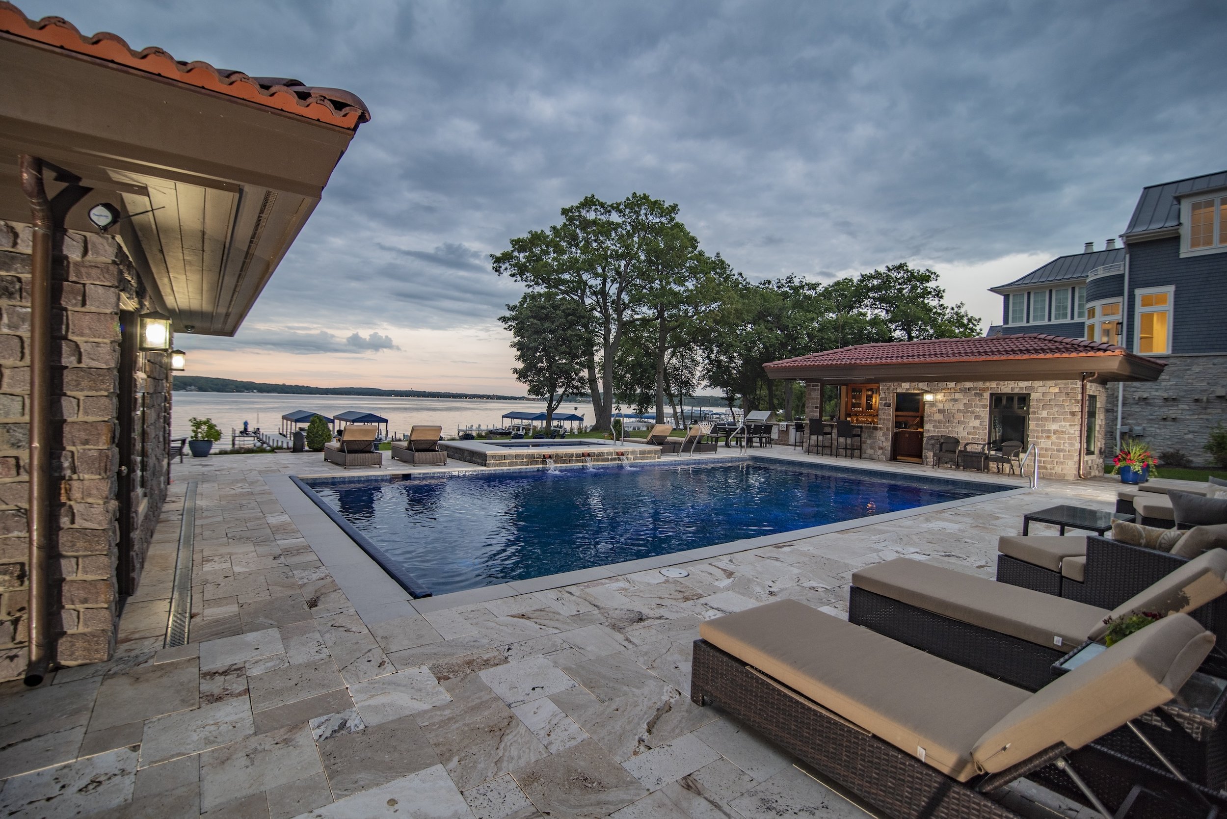 Luxurious backyard with swimming pool, patio, lounge chairs, and a view of a lake