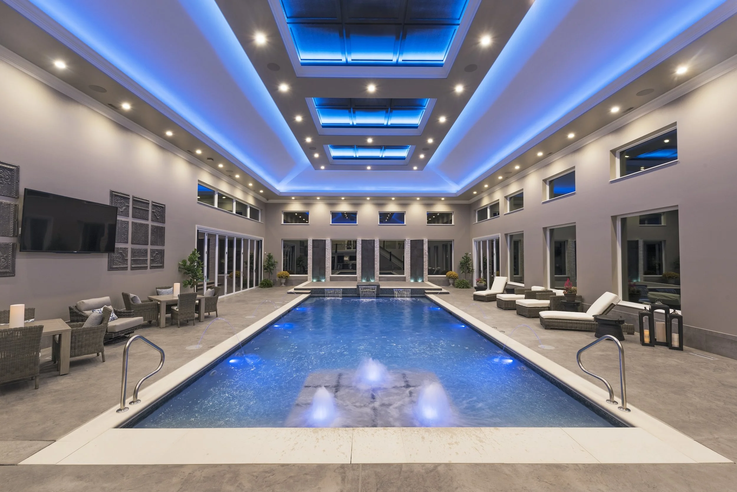 Luxury indoor swimming pool with modern seating, blue LED lighting, and high ceiling.