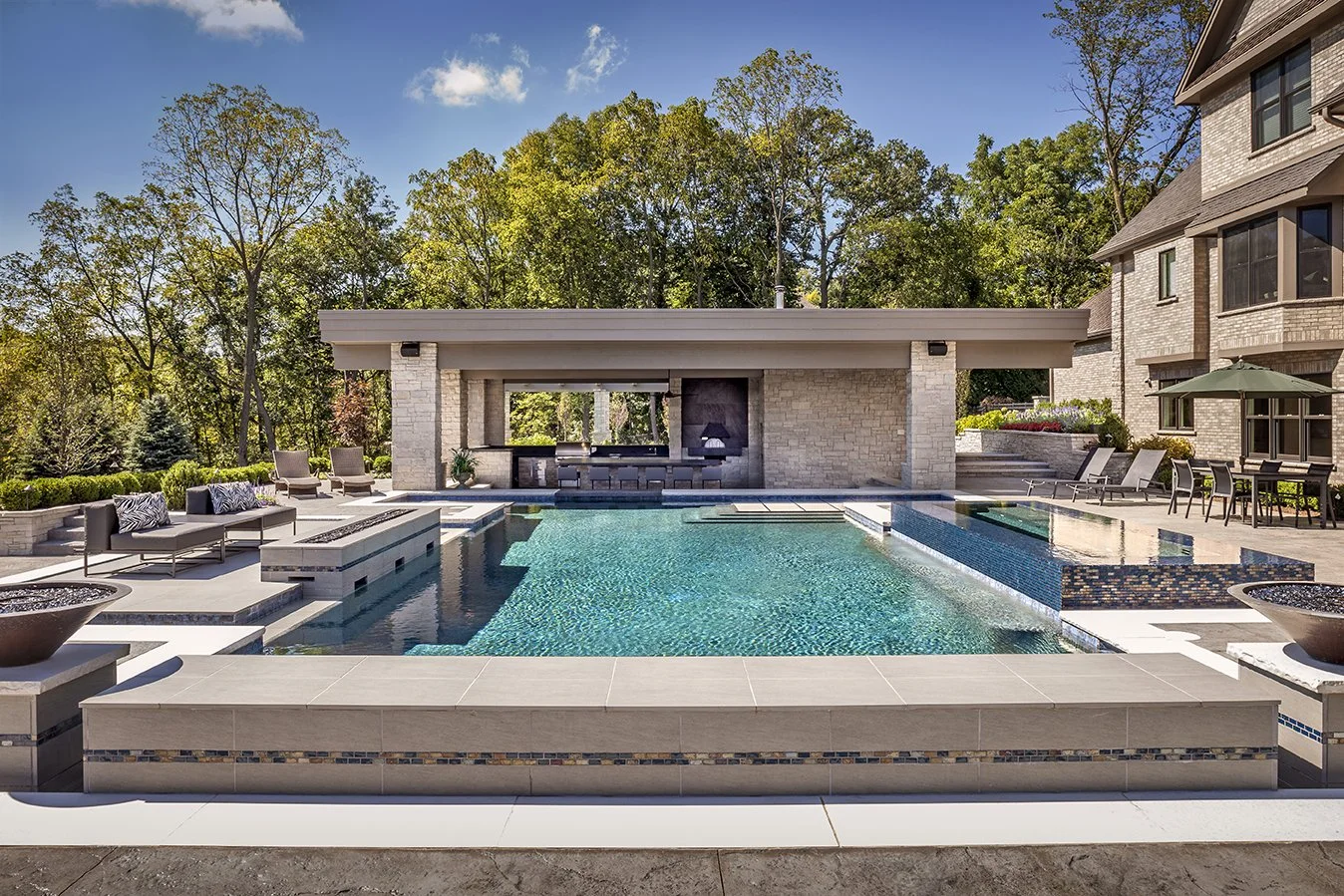 Luxurious backyard with a large modern swimming pool, surrounding patio, lounge chairs, and trees in the background.