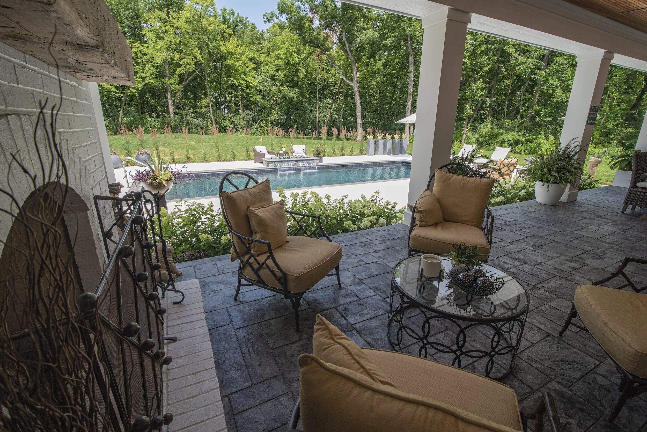 Outdoor patio with chairs and table overlooking lawn and pool