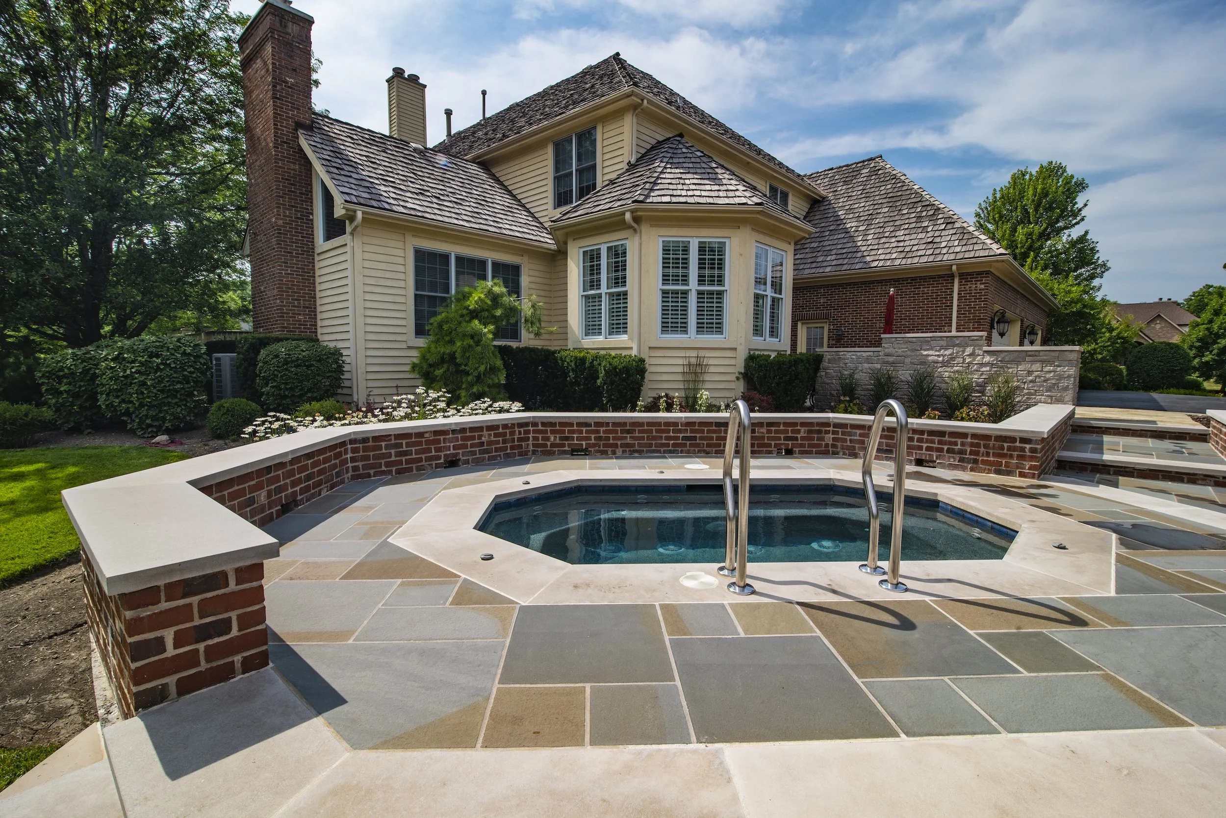 Backyard with a patio, hot tub, and a traditional style house with wooden siding and a brick chimney.