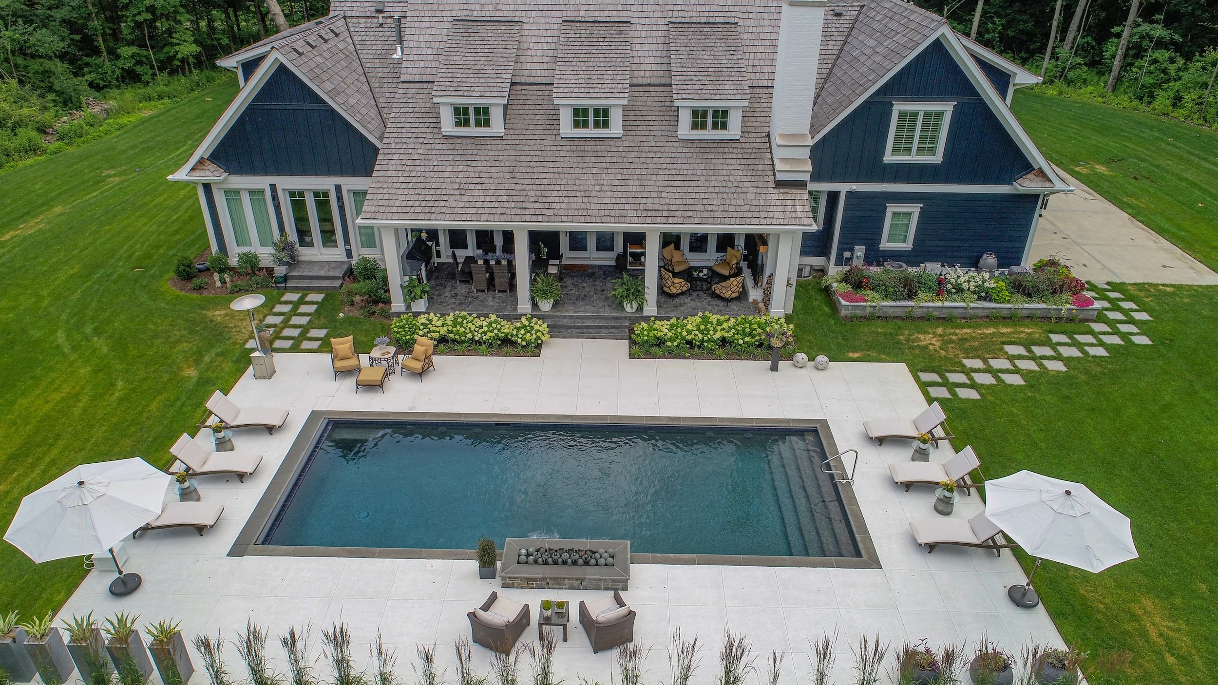 Aerial view of a modern house with a backyard pool, patio seating, and manicured lawn.