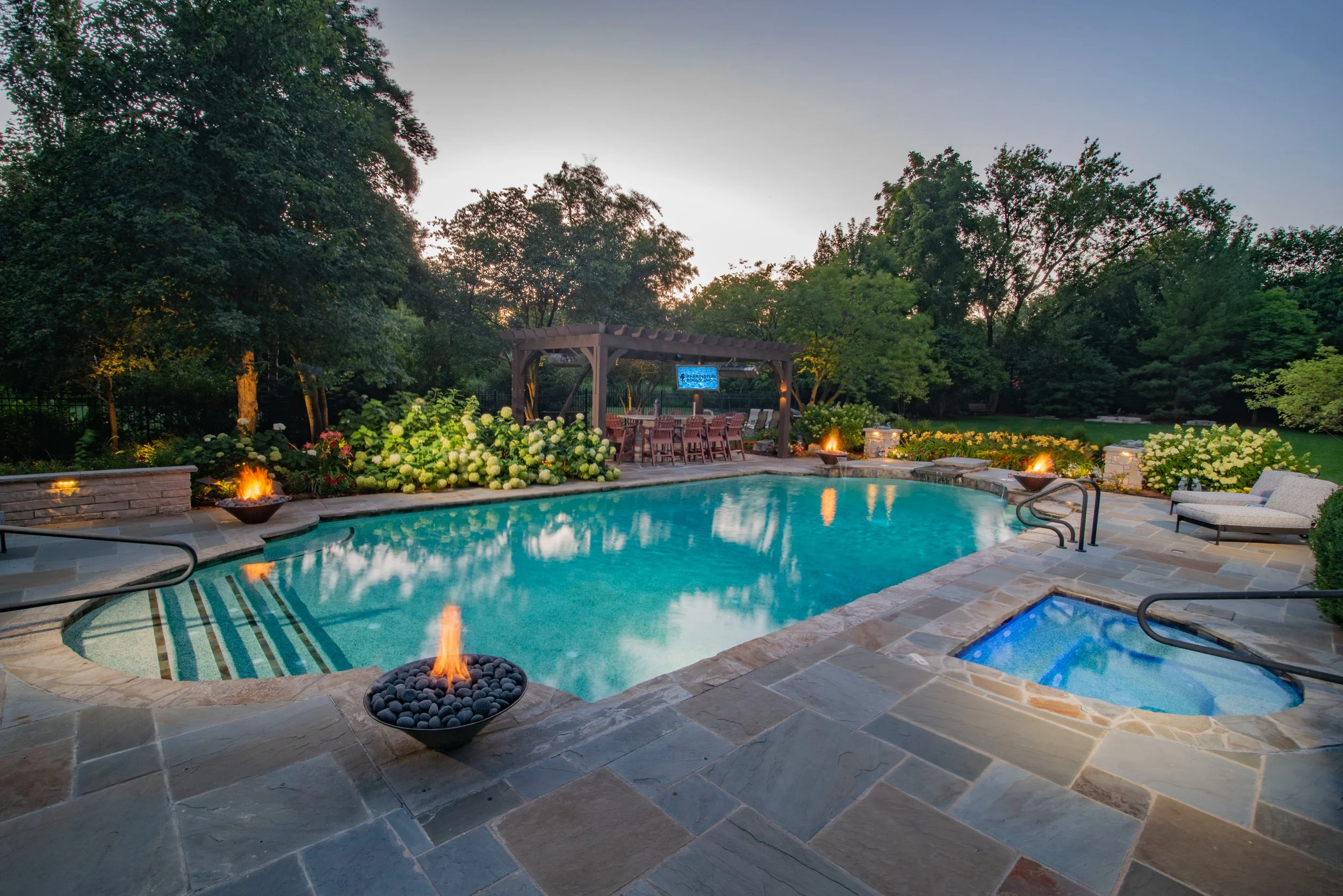 A luxurious backyard swimming pool area with a pergola, seating, greenery, and fire pits.