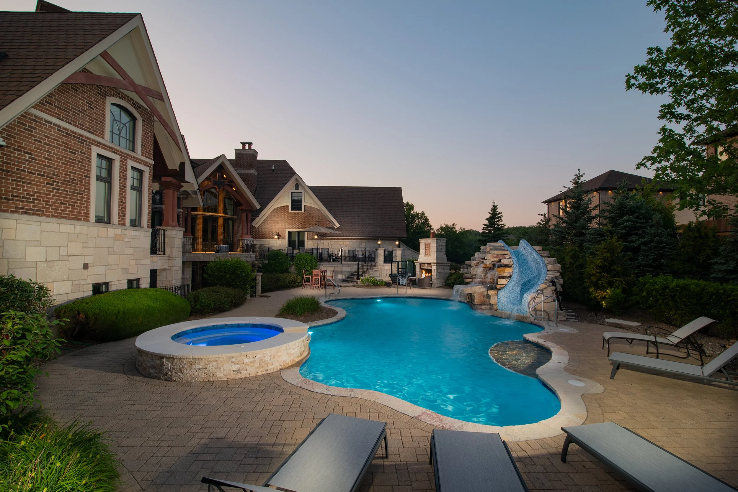 Luxurious Barrington Pools inground pool at dusk with spa and mosaic tile waterslide