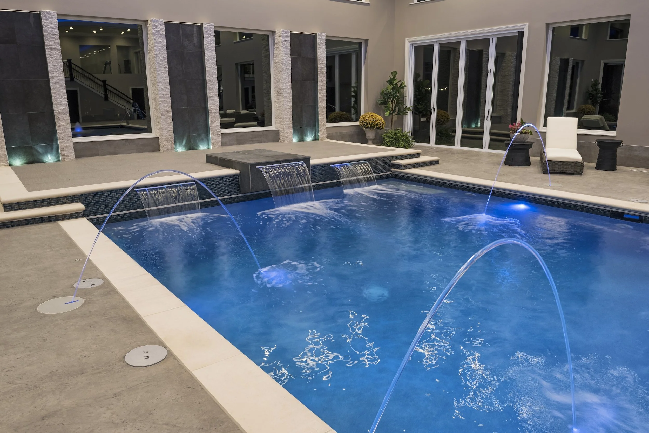 Luxury indoor swimming pool with water fountains, modern design, and poolside seating.
