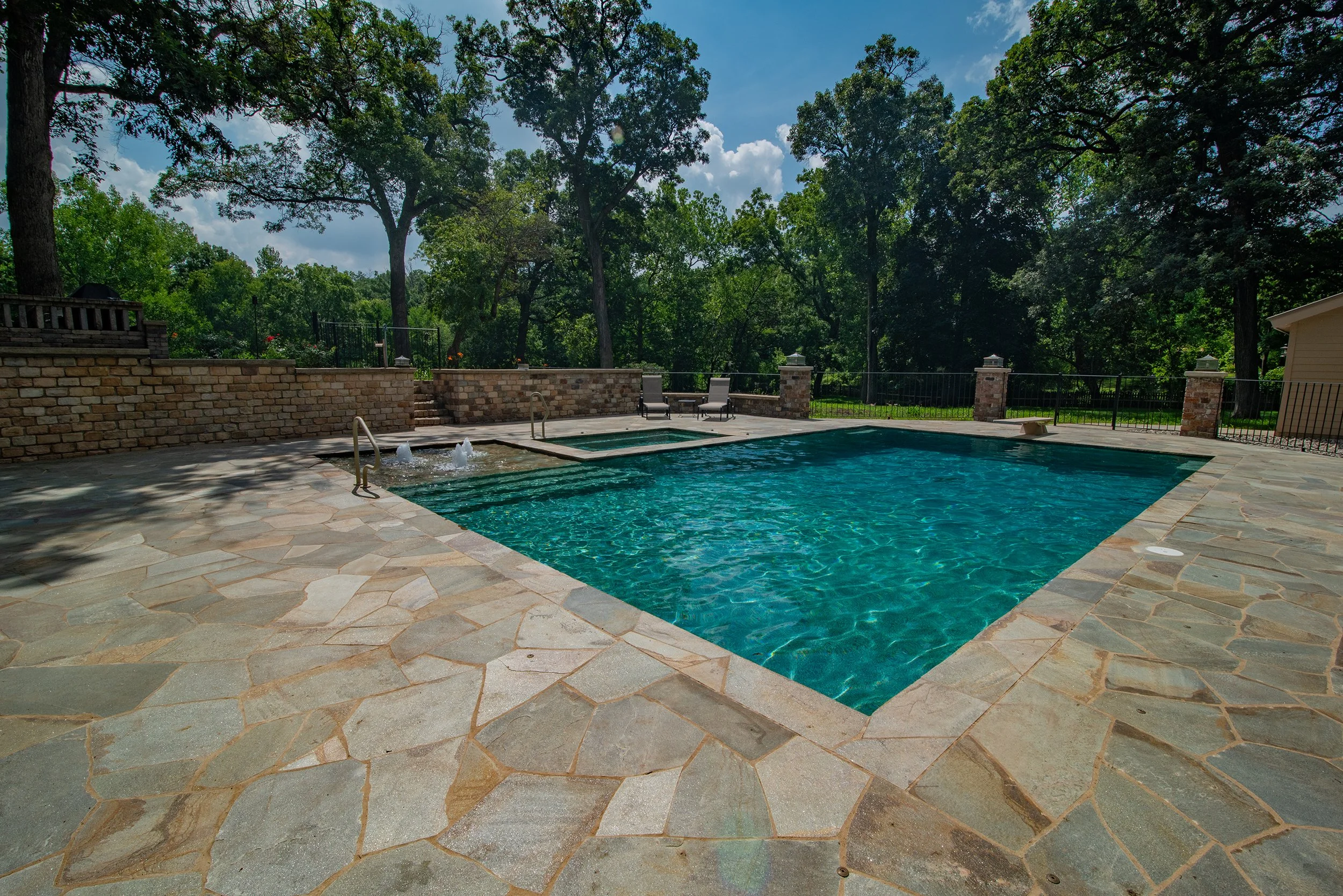 A modern shotcrete inground pool native stone deck bubblers and tanning ledge with large custom spa