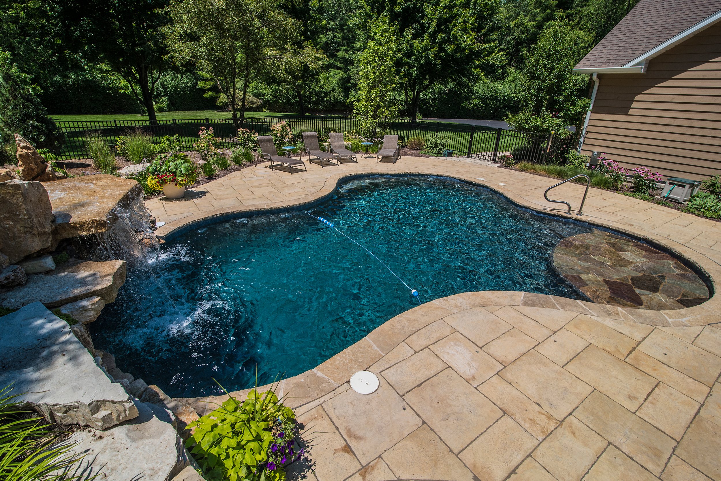 Luxurious shotcrete inground pool built by Barrington Pools with dramatic waterfall, tanning ledge, and lush landscaping