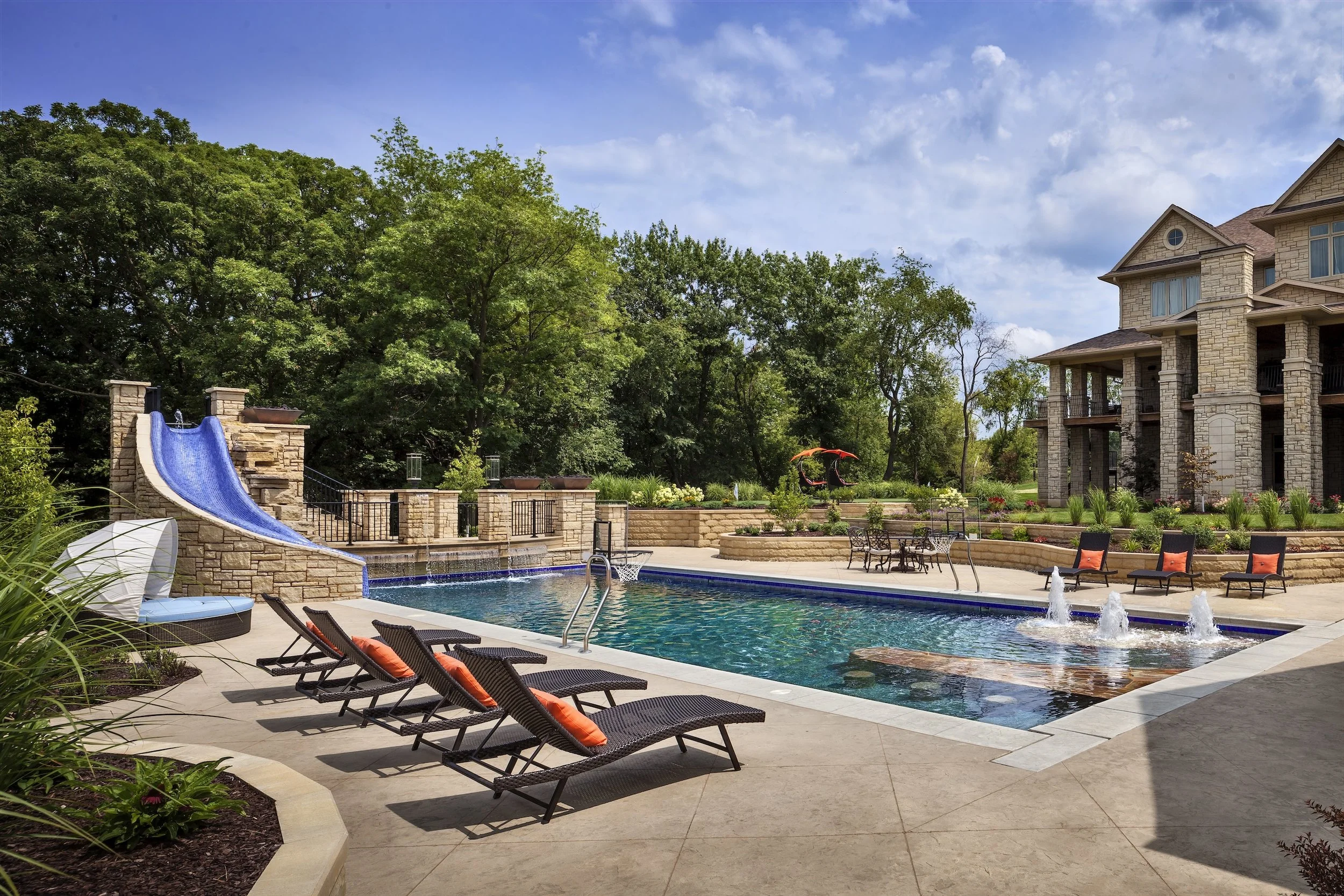 Luxury backyard with swimming pool, water slide, loungers, and landscaping.
