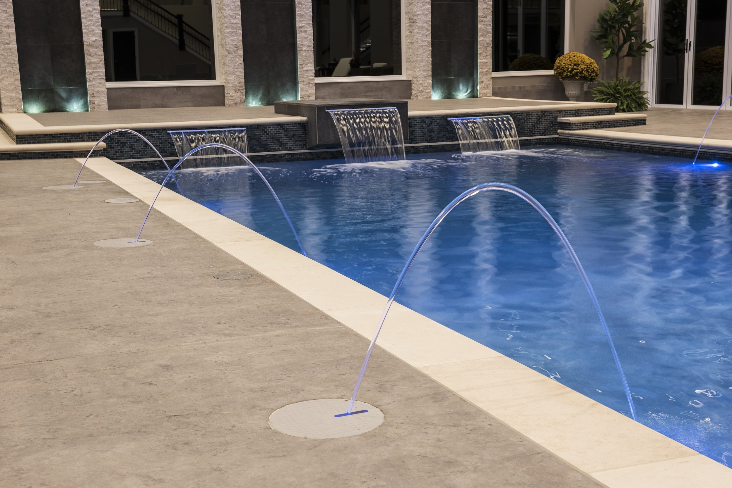 Luxury swimming pool with water fountains and deck at night