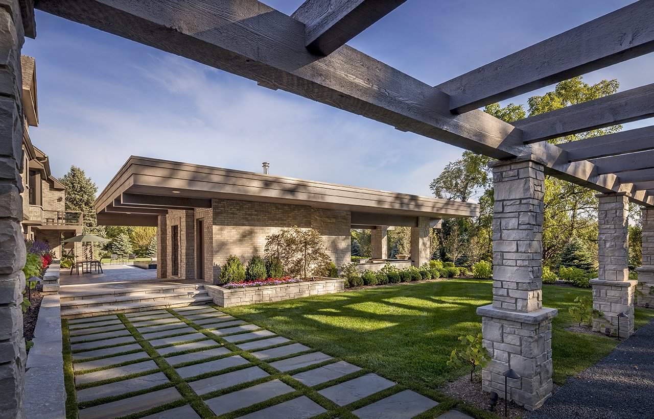 Modern house with stone pillars, a pergola, manicured lawn, and pathway.