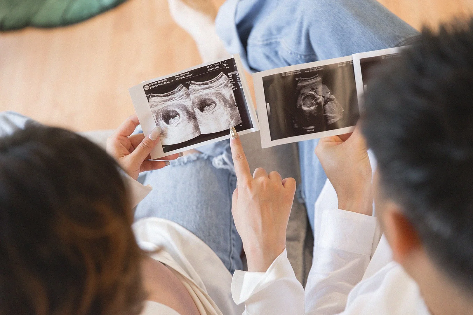 Two people, likely medical professionals, looking at ultrasound images of a fetus. One person points at the images, which show black and white scans of a developing baby inside a womb.